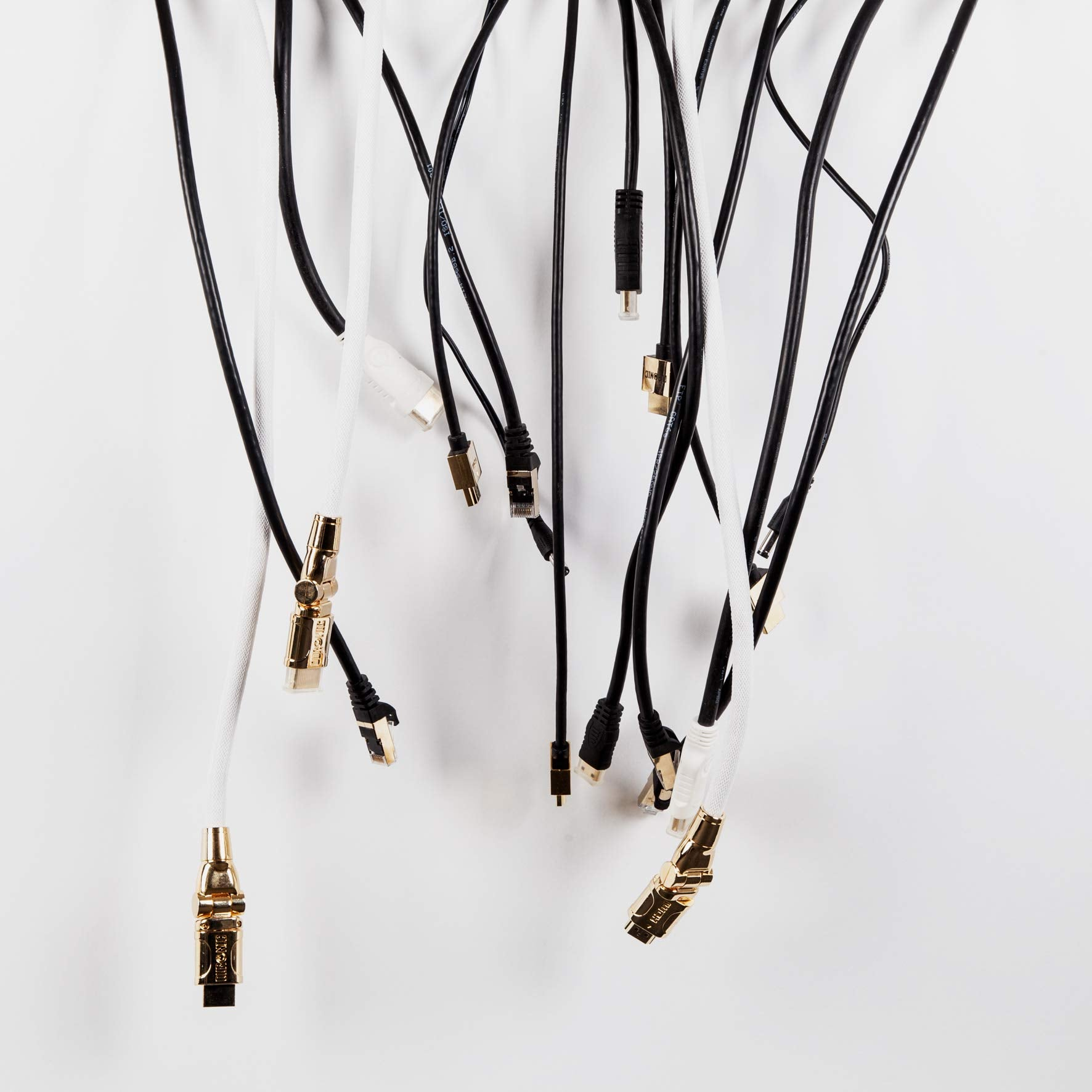 Múltiples cables con varios conectores cuelgan sobre un fondo blanco. Cables negros y blancos.