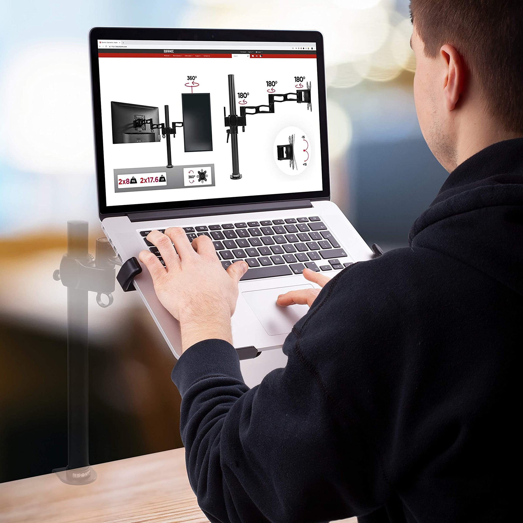 Ein Mann benutzt einen Laptop auf einem Schreibtisch, verbunden mit einer Monitorhalterung, die Bilder eines Monitors anzeigt.