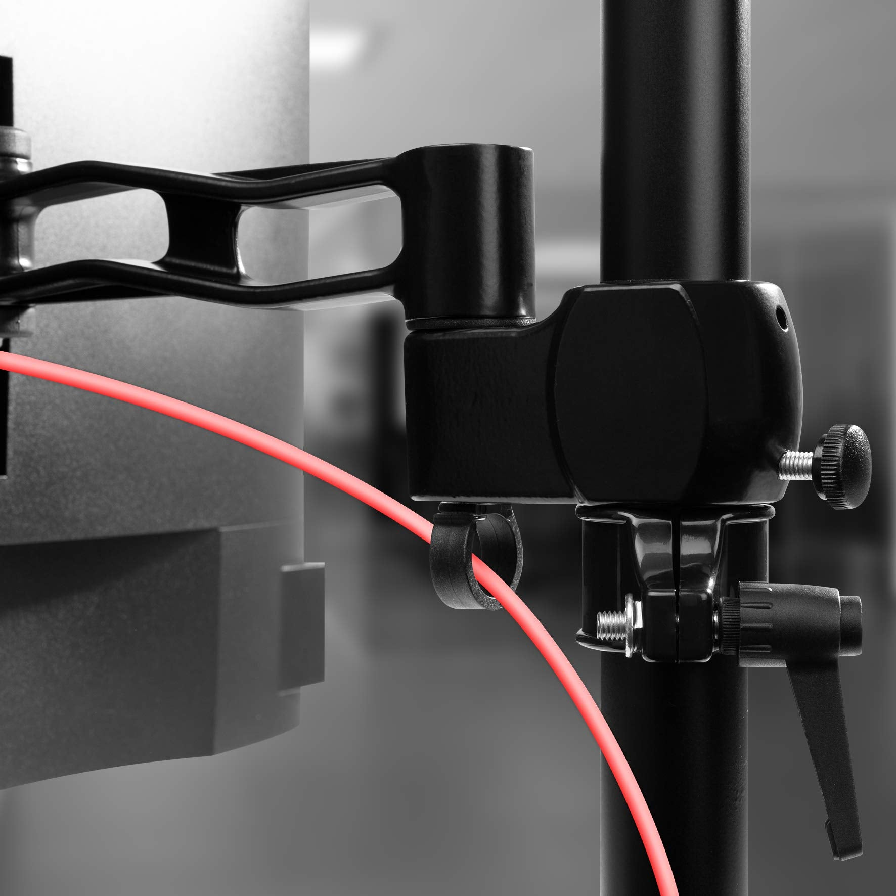 Schwarze Metall-Monitorhalterung mit rotem Kabel. Der Ständer ist an einer schwarzen Stange befestigt.