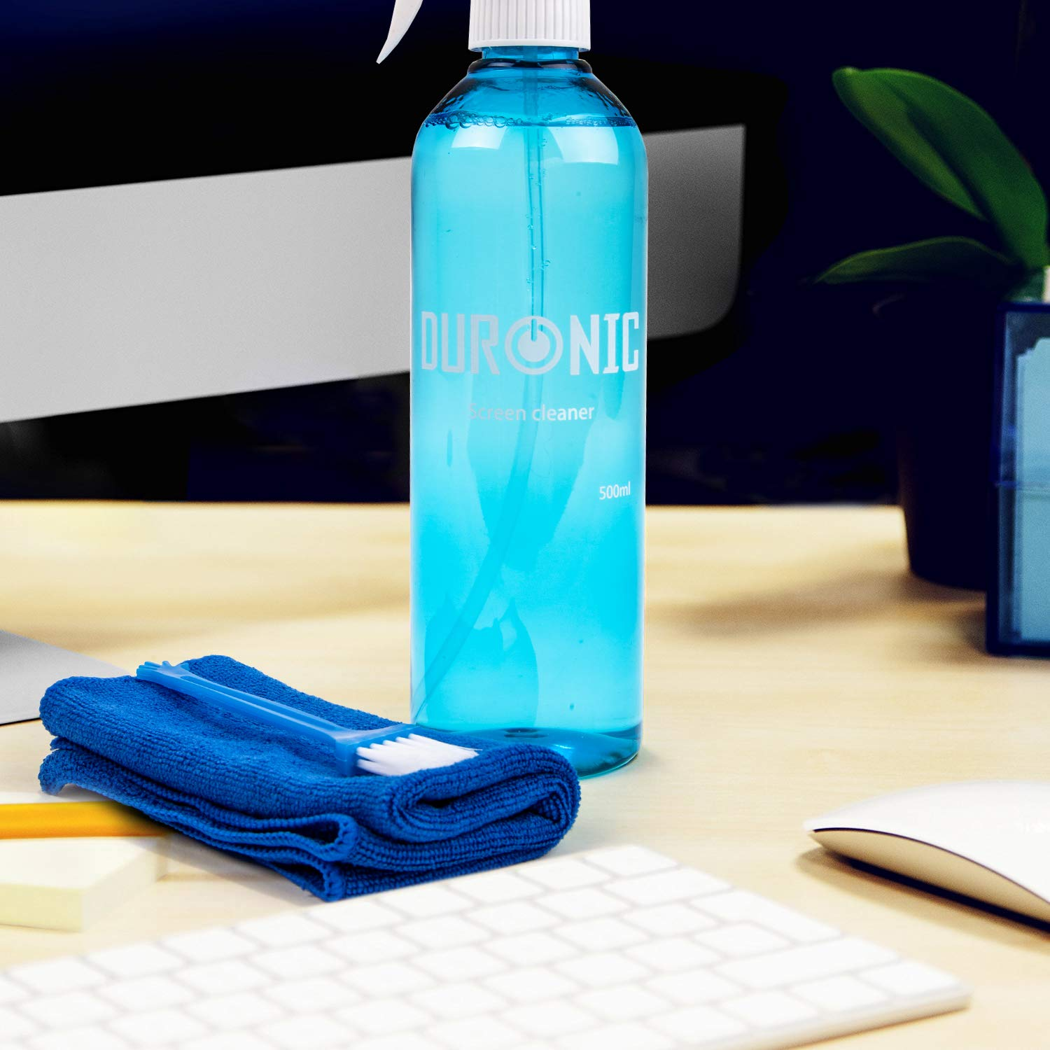 Eine Flasche blauen Bildschirmreinigers, ein blaues Mikrofasertuch und eine Bürste auf einem Holzschreibtisch.