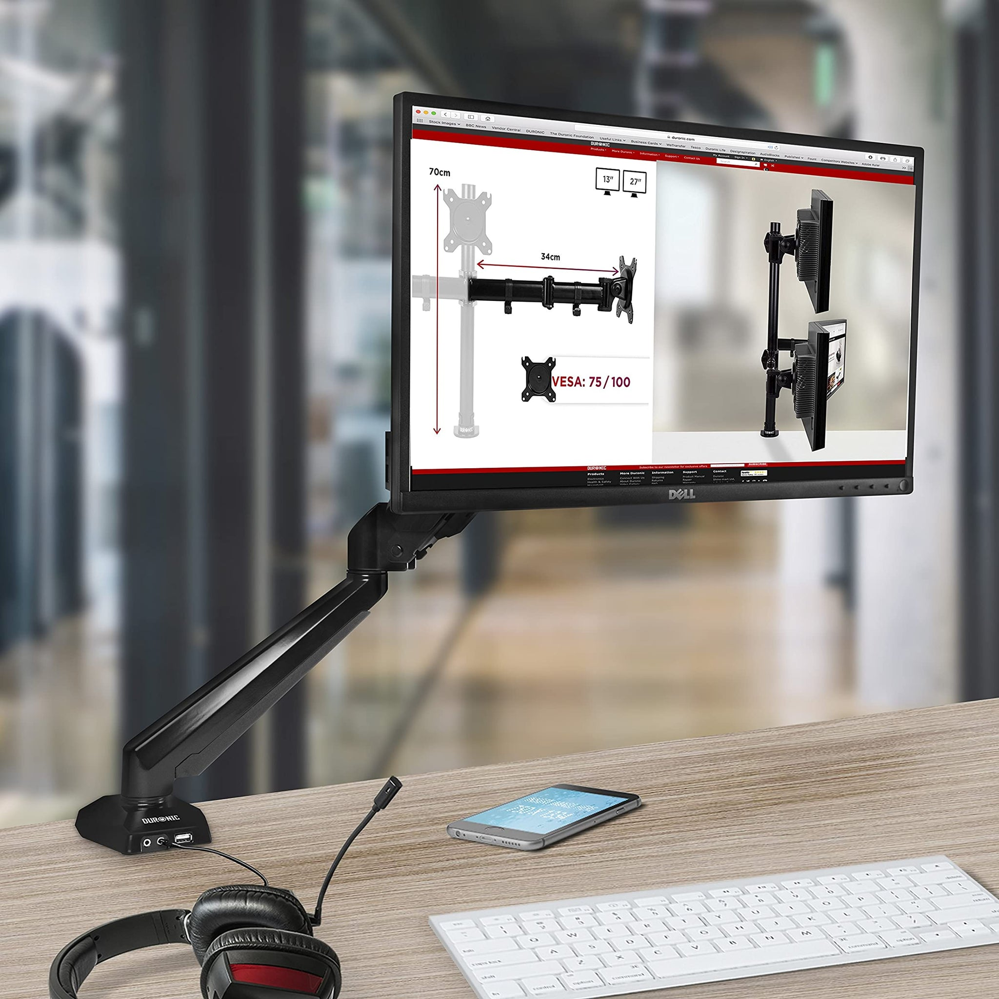 Ein Monitor, der auf einem Schreibtisch mit einem Ständer mit verstellbaren Armen, Tastatur, Headset und Telefon montiert ist.