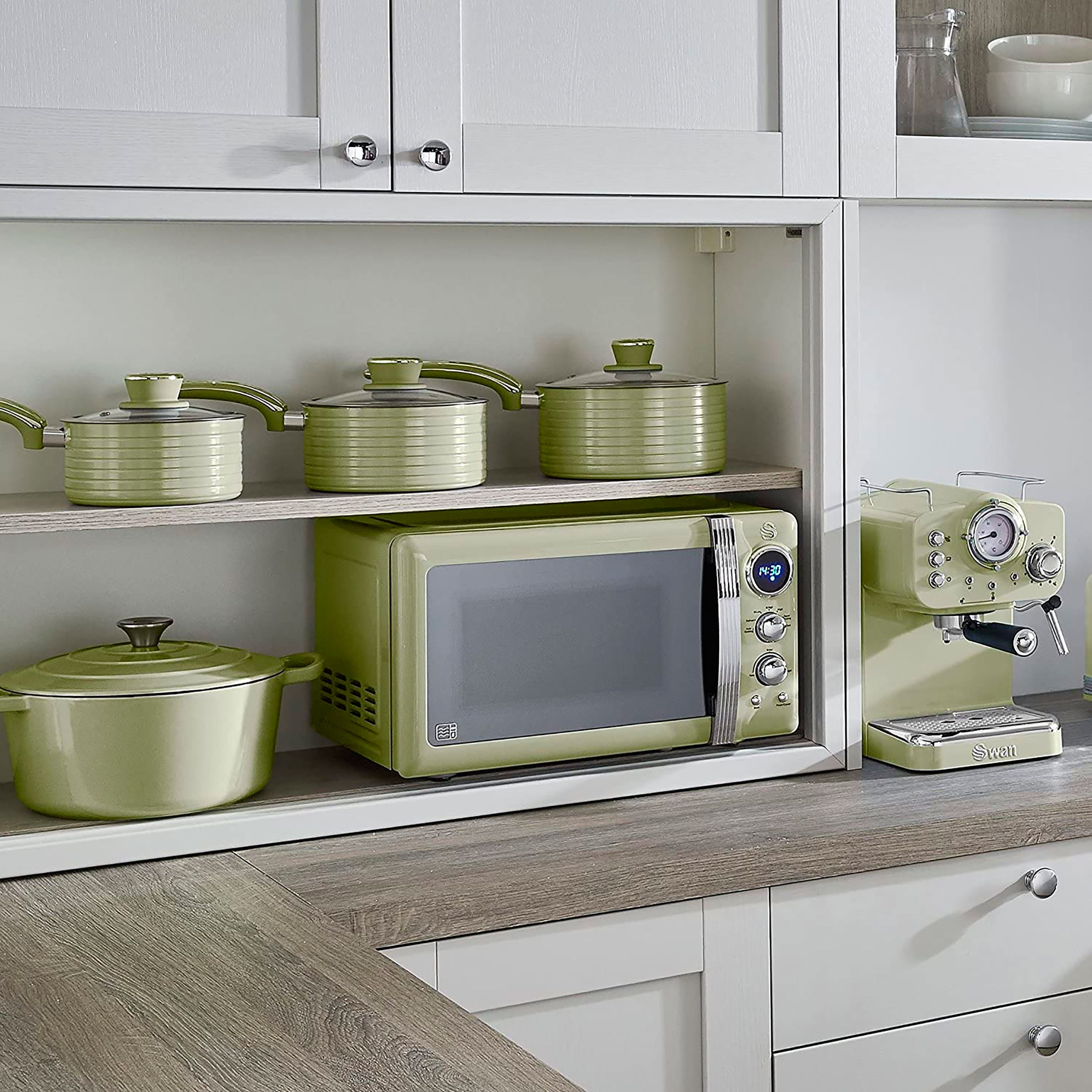 Grüne Küche mit Mikrowelle, Töpfen und Espressomaschine auf Holztheke in weißen Schränken.