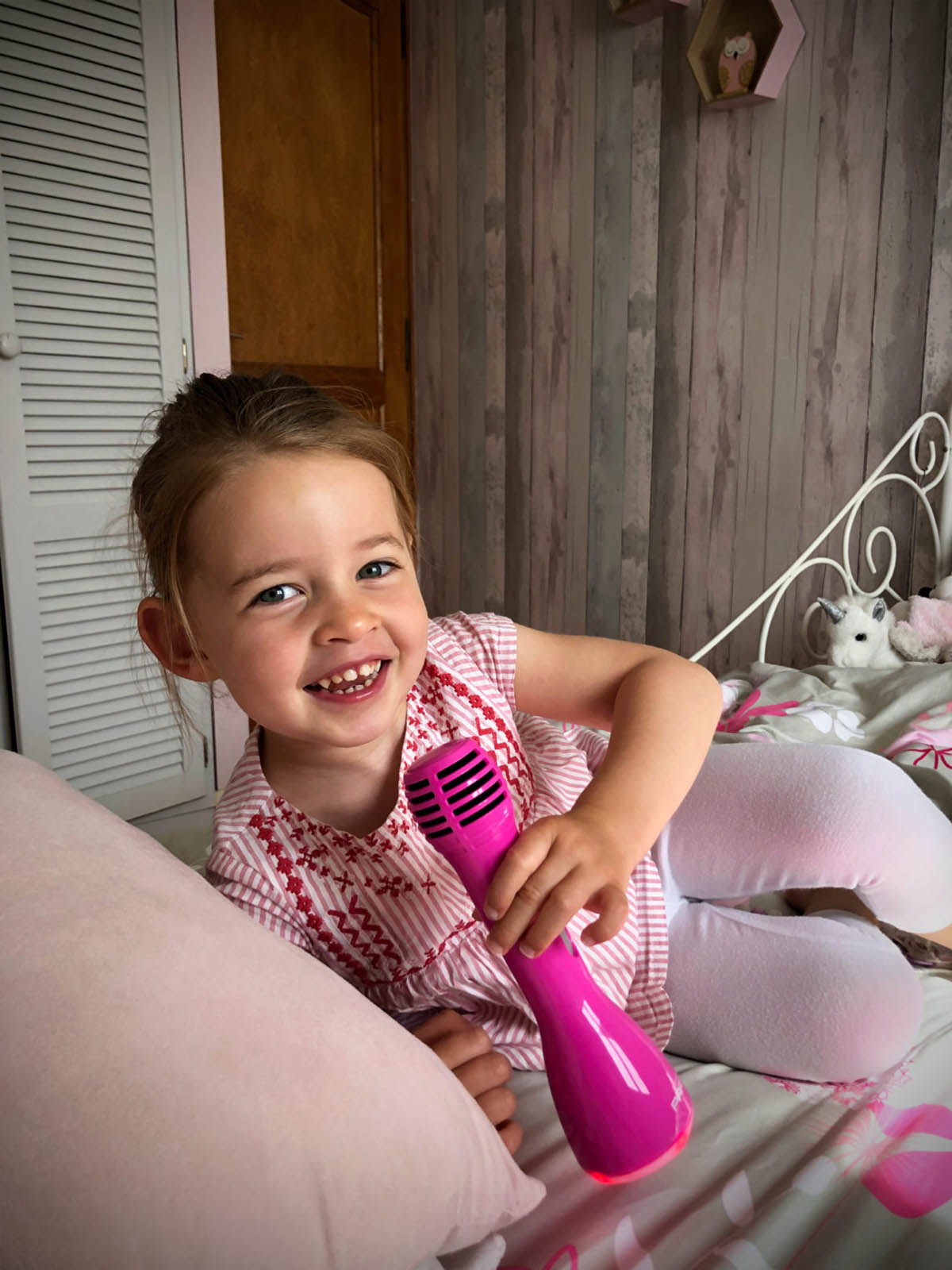 Ragazza sorridente, tiene un microfono rosa a letto.