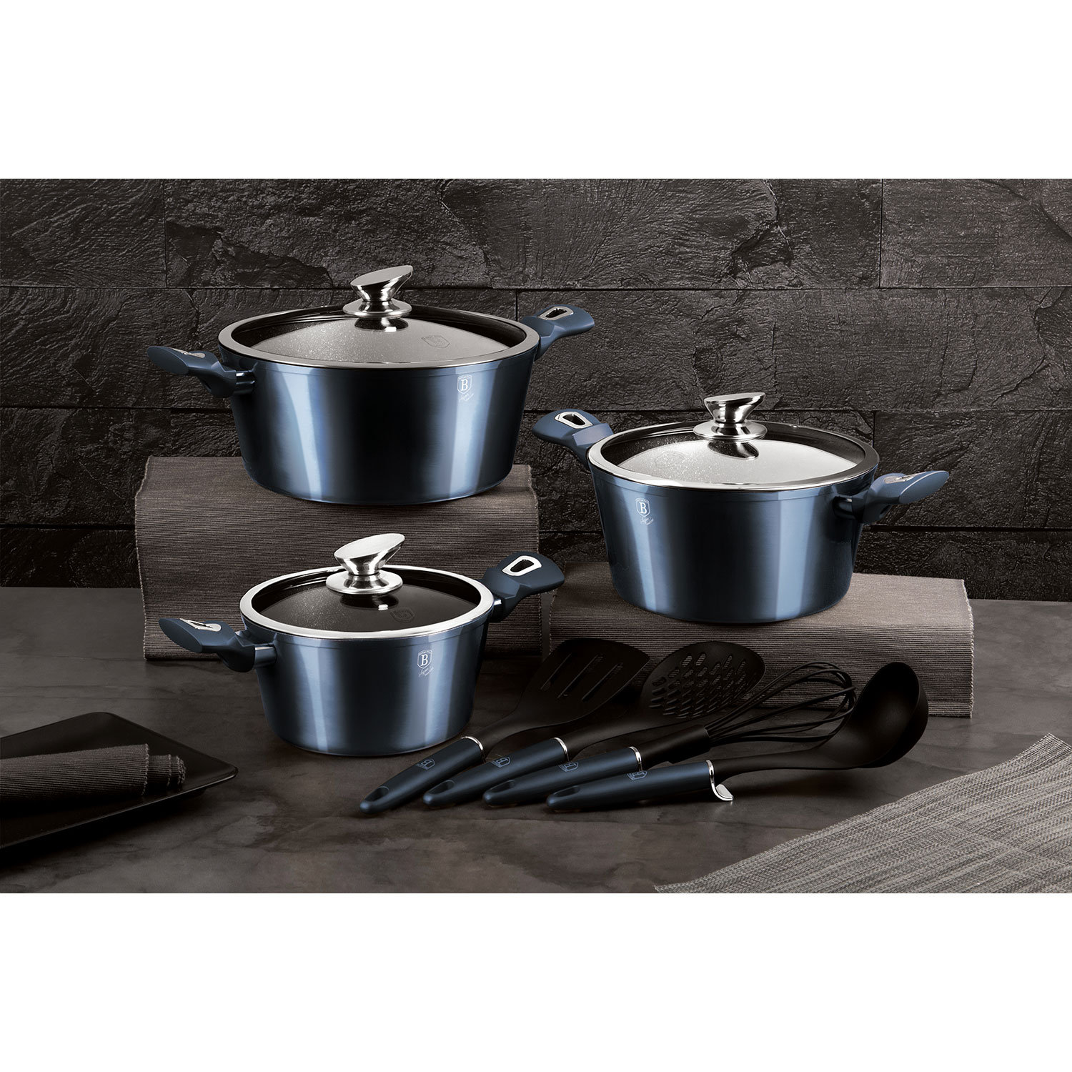 Un juego de tres ollas azules y utensilios de cocina sobre una superficie oscura.