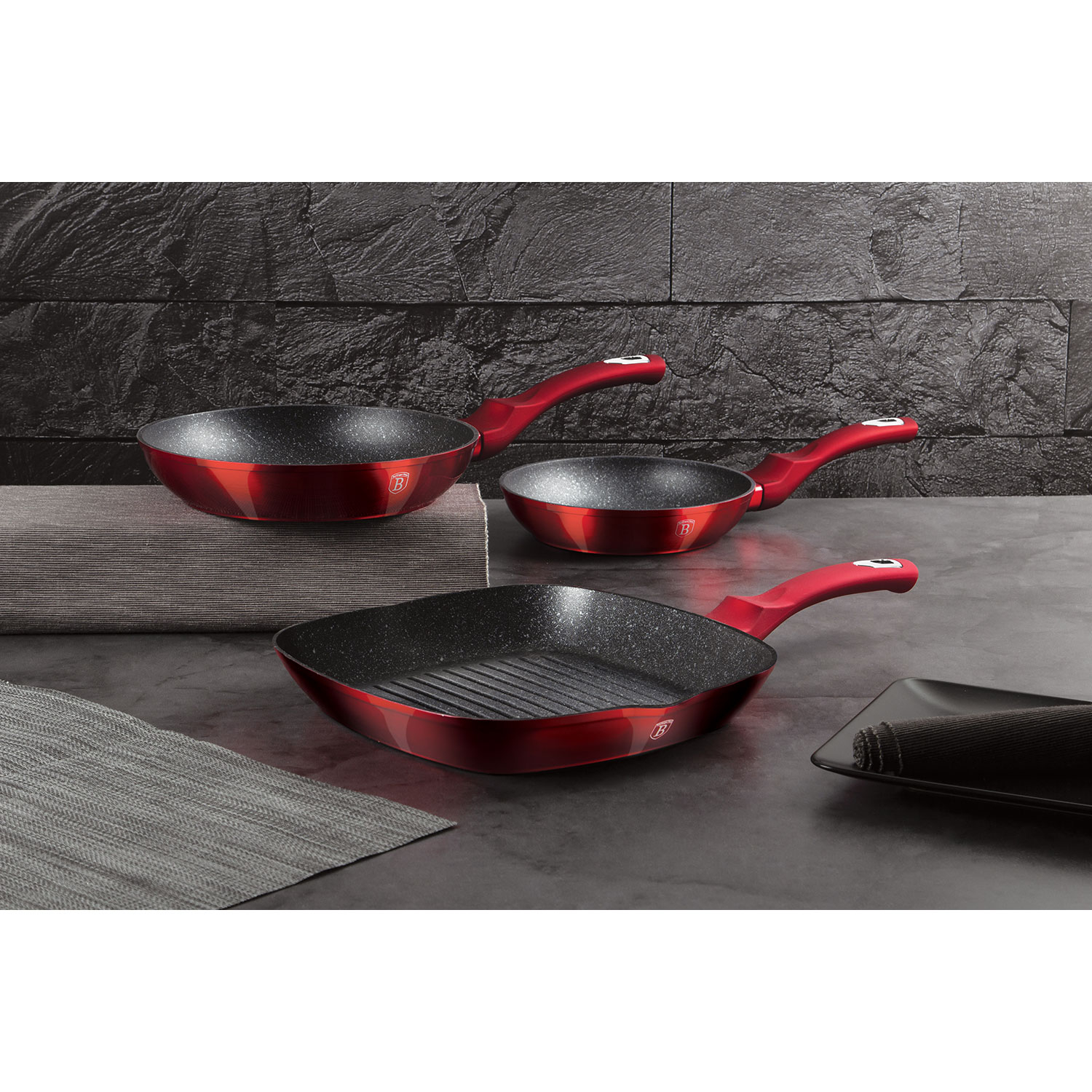 Tres sartenes rojas con mangos rojos sobre fondo oscuro. Una es cuadrada.