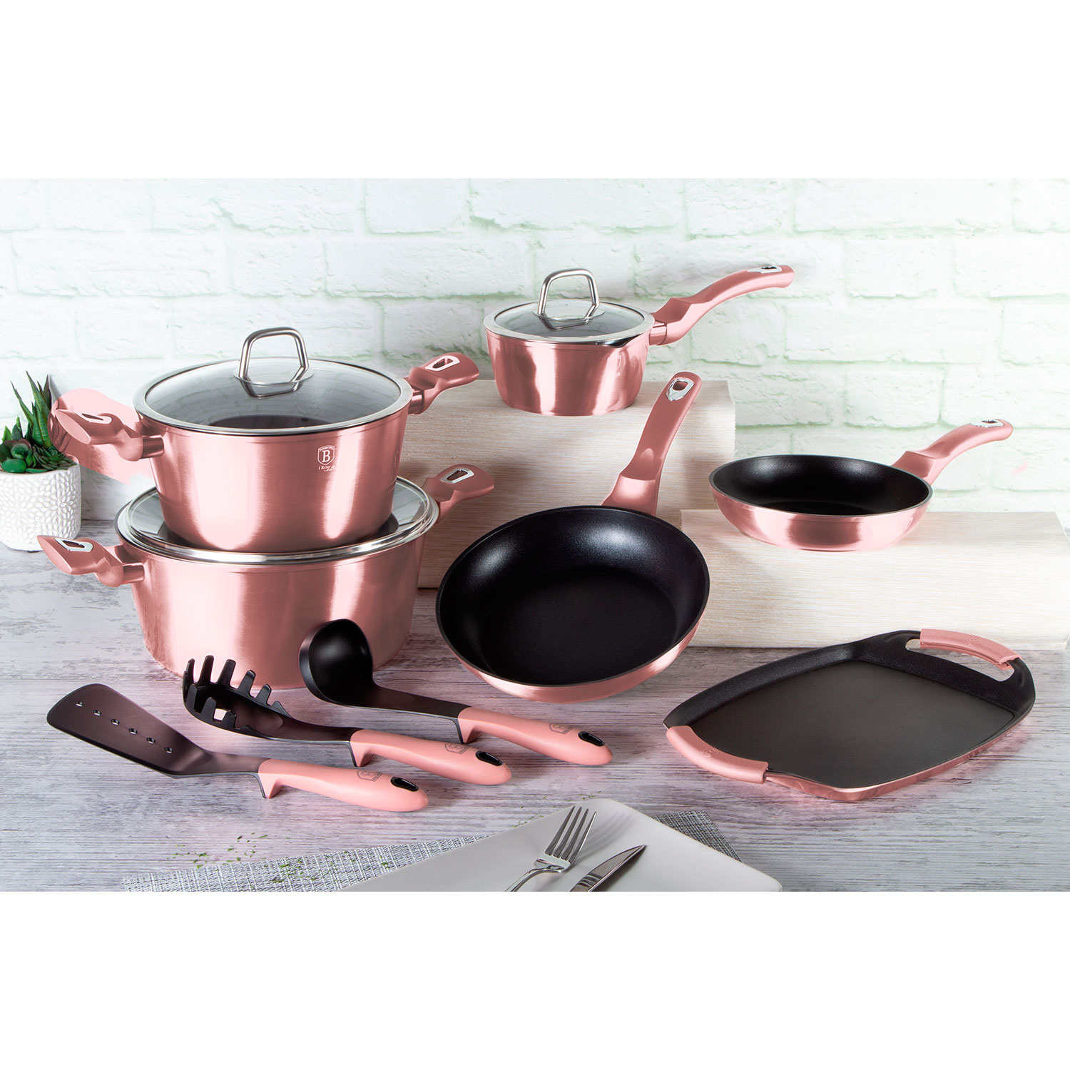 Juego de utensilios de cocina color oro rosa sobre una superficie blanca. Incluye ollas, sartenes y utensilios.