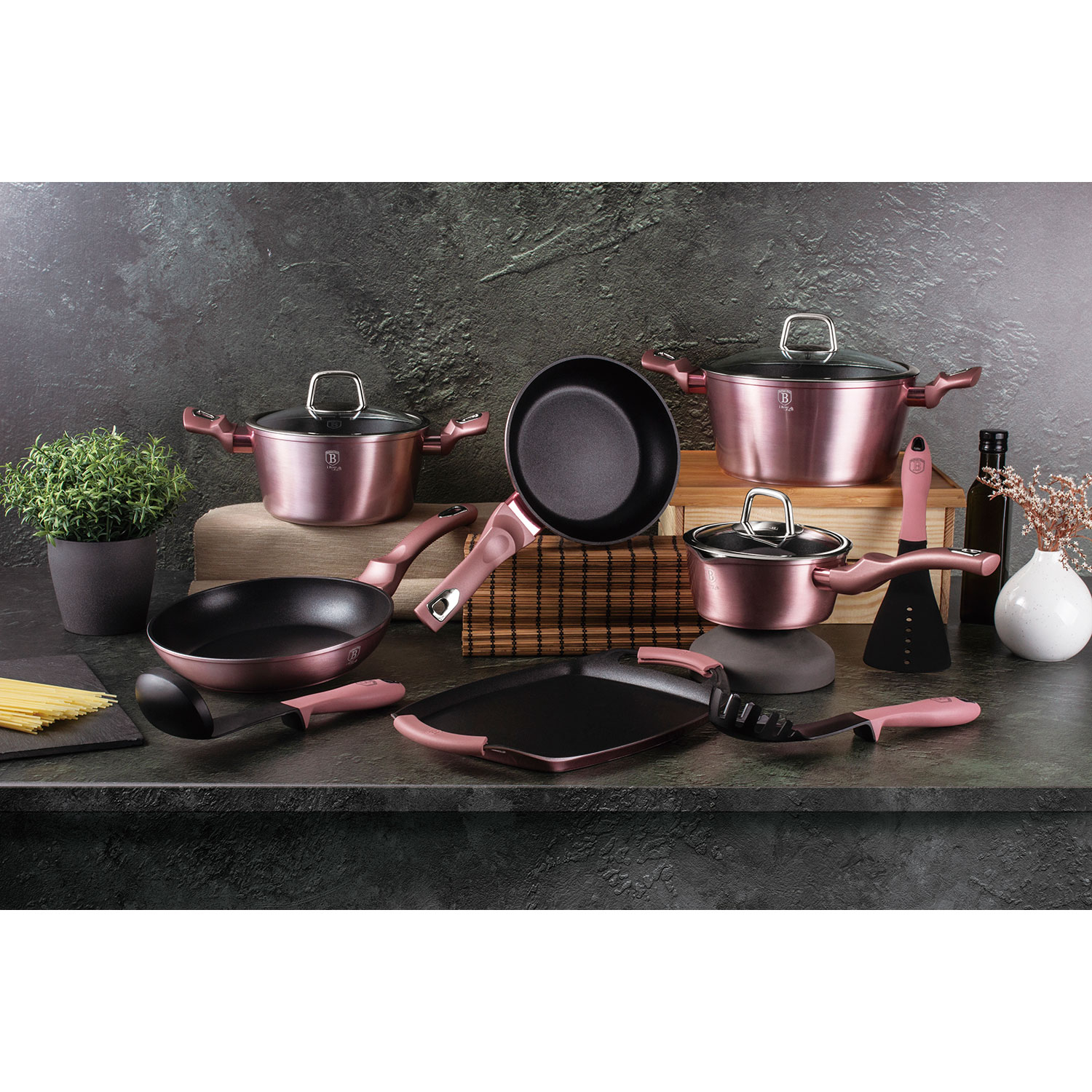 Juego de utensilios de cocina. Ollas, sartenes y utensilios en color oro rosa. Todo está dispuesto sobre una superficie oscura.