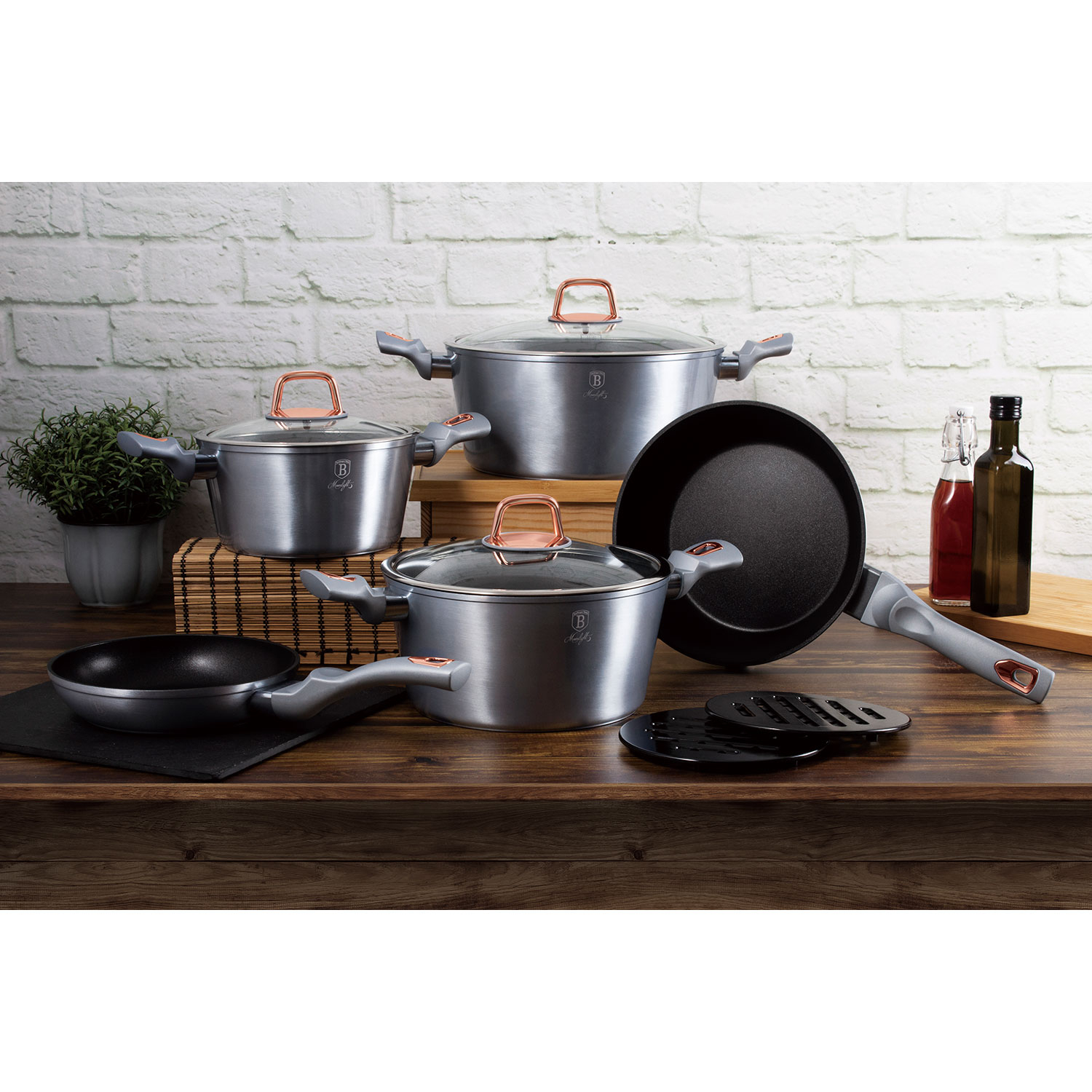 Juego de utensilios de cocina en mesa de madera. Incluye ollas, sartenes y accesorios. Fondo de ladrillo.