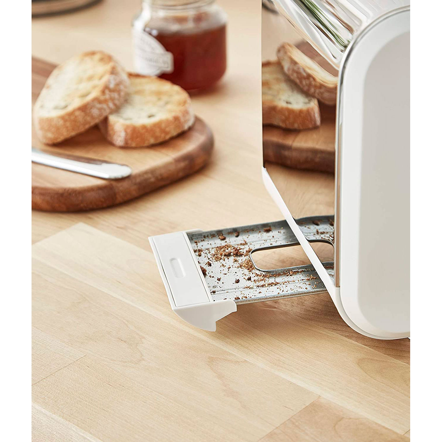 Toaster mit Brot darin. Brotscheiben auf einem Holzbrett mit einem Messer und einem Glas Marmelade im Hintergrund.