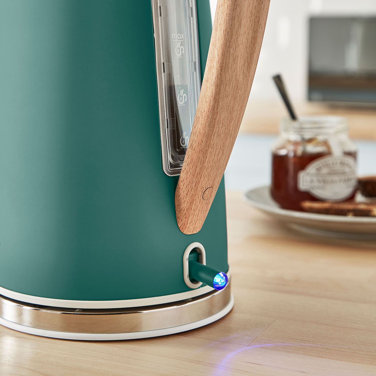 Ein grüner Wasserkocher mit Holzgriff, blauem Licht am Fuß und Marmeladenglas.
