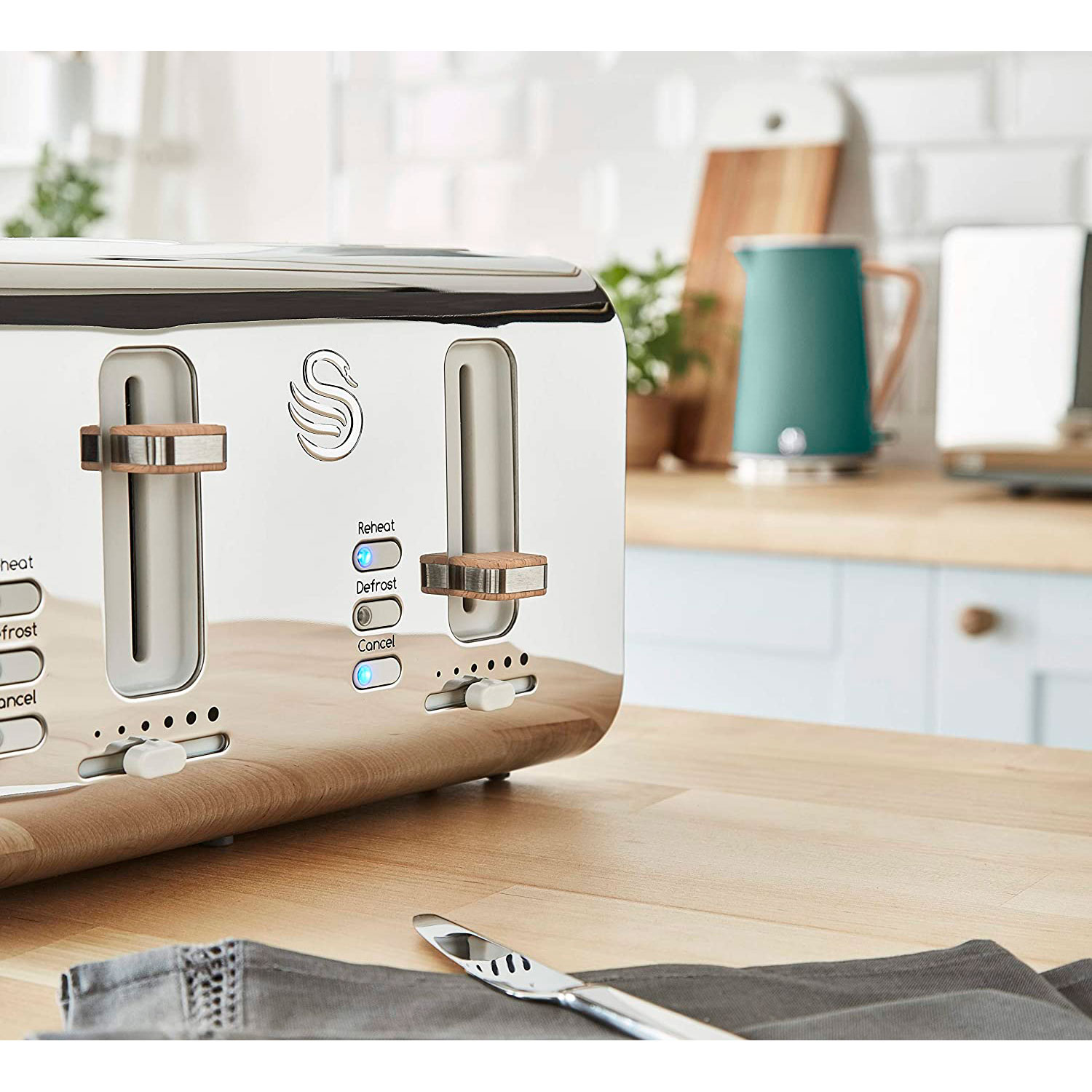 Silberner Toaster mit Holzakzenten auf einer Holzplatte, mit einem türkisfarbenen Wasserkocher im Hintergrund.