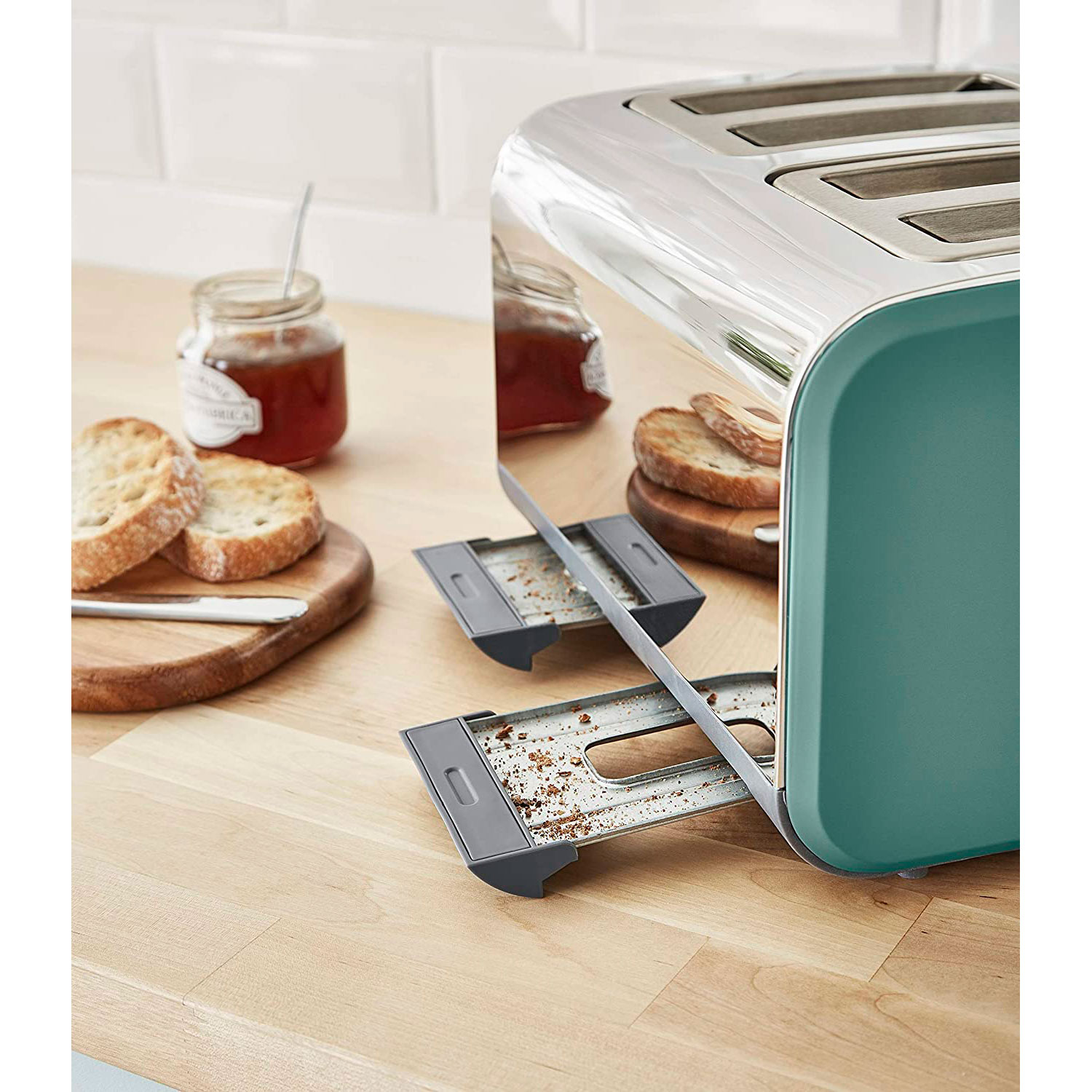 Toaster mit Brot und Marmelade auf Holzbrettern. Der Toaster ist türkis. Der Hintergrund ist eine Küche.