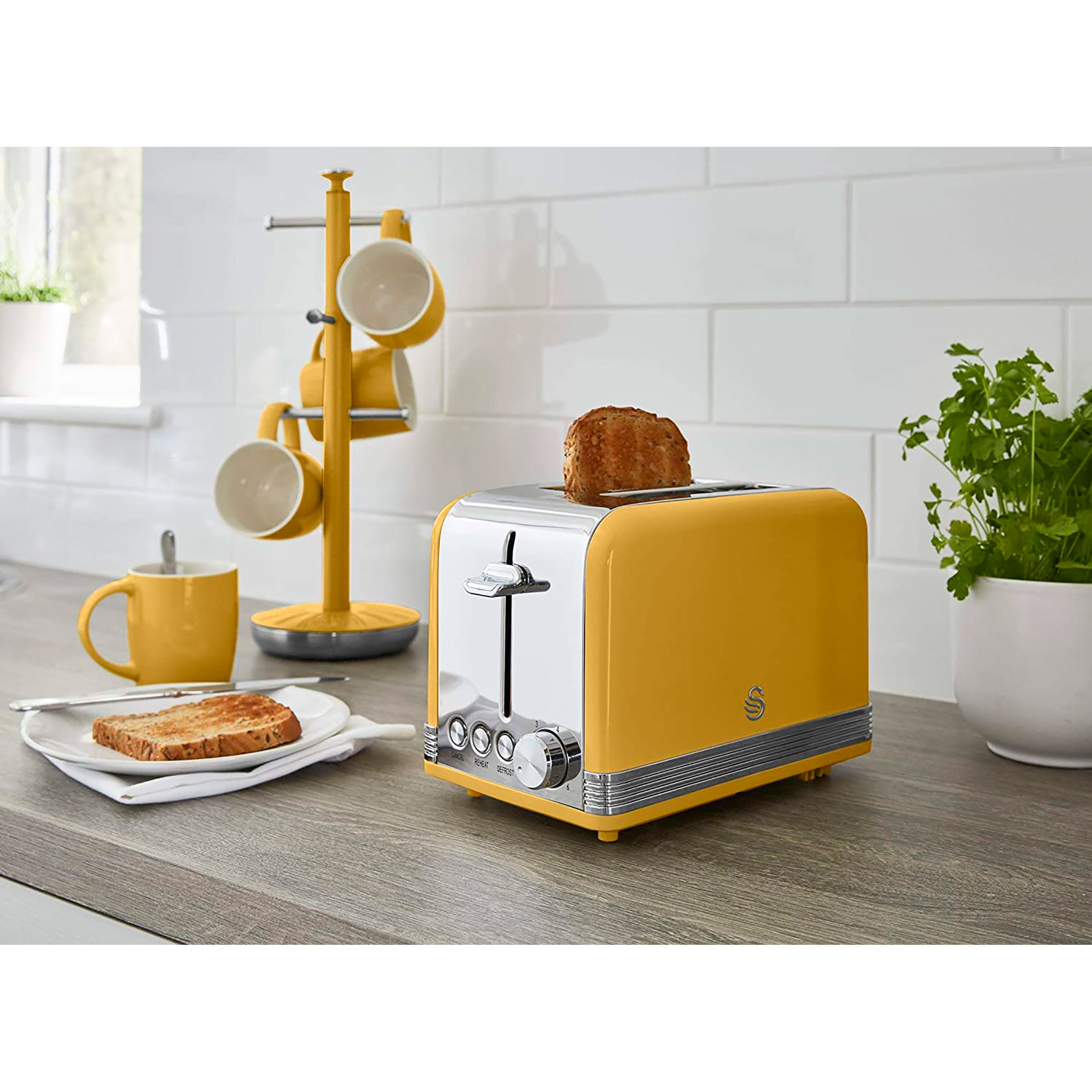 Gelber Toaster mit Toastscheibe. Ein Becherbaum und Tassen sind im Hintergrund.