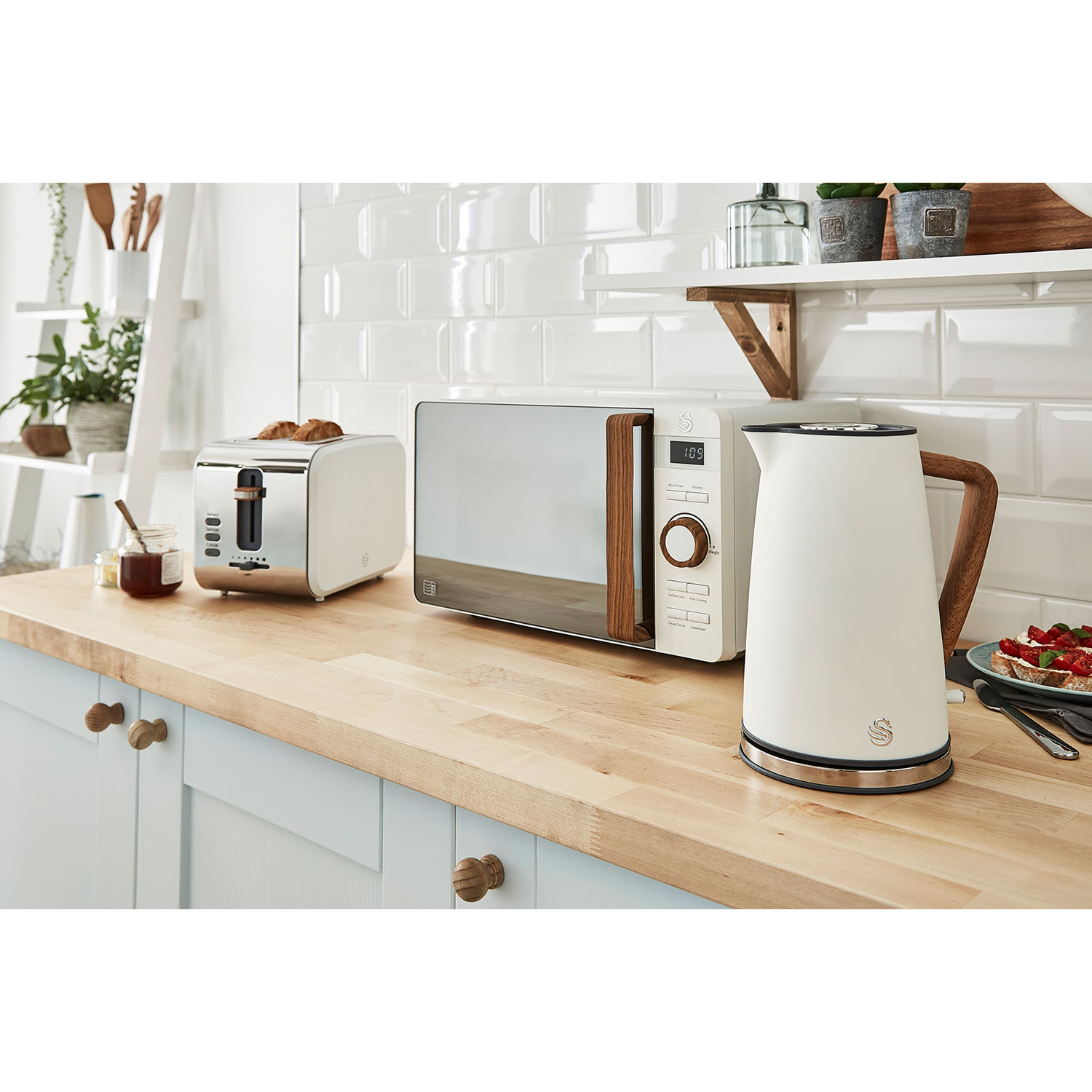 Küchenszene mit weißem Wasserkocher, Toaster und Mikrowelle auf einer Holztheke.