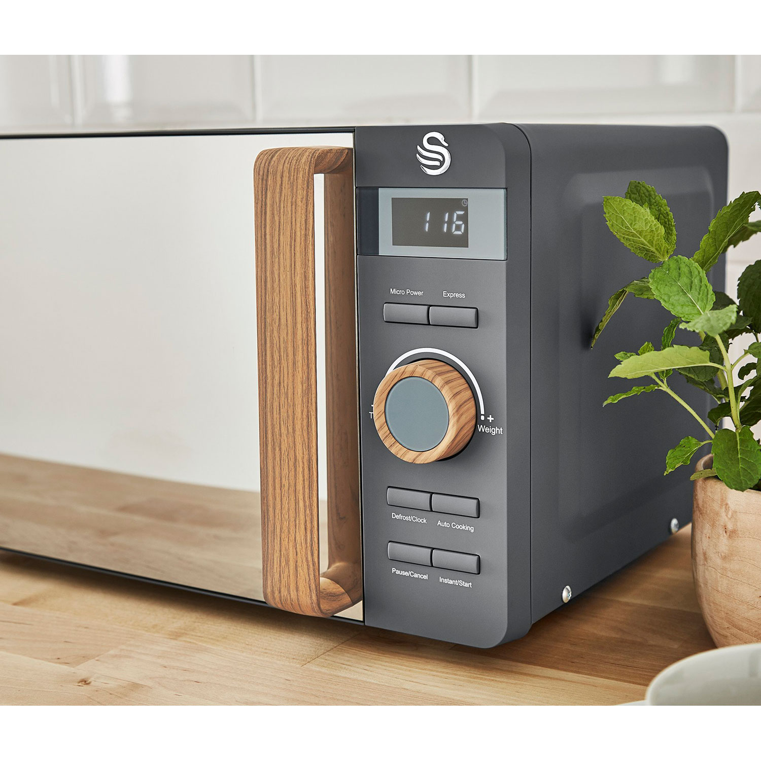 Mikrowelle, grau mit Holzgriff. Digitalanzeige und Knöpfe. Pflanze im Topf auf der Theke.