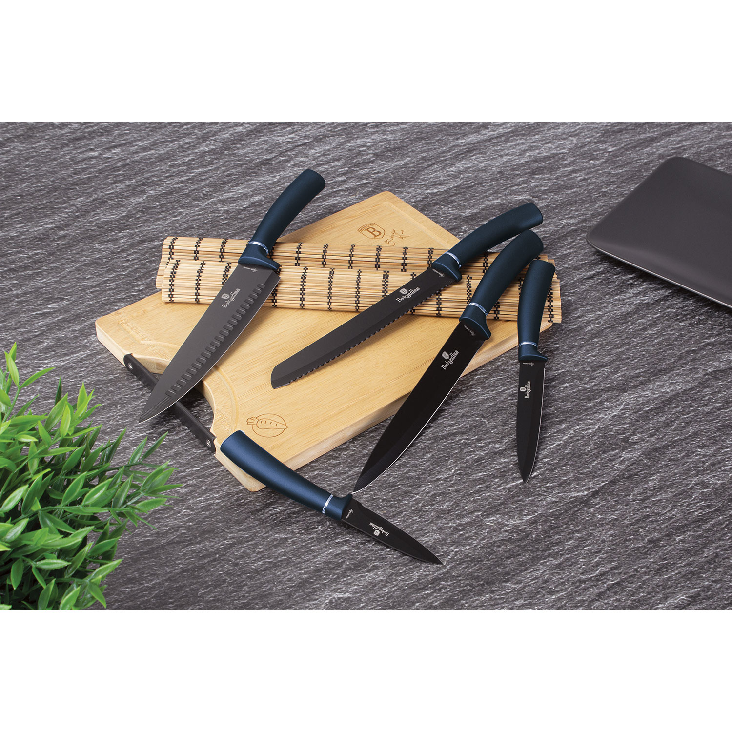 Juego de cuchillos con mangos azules sobre una tabla de cortar de madera, con superficie gris oscura.
