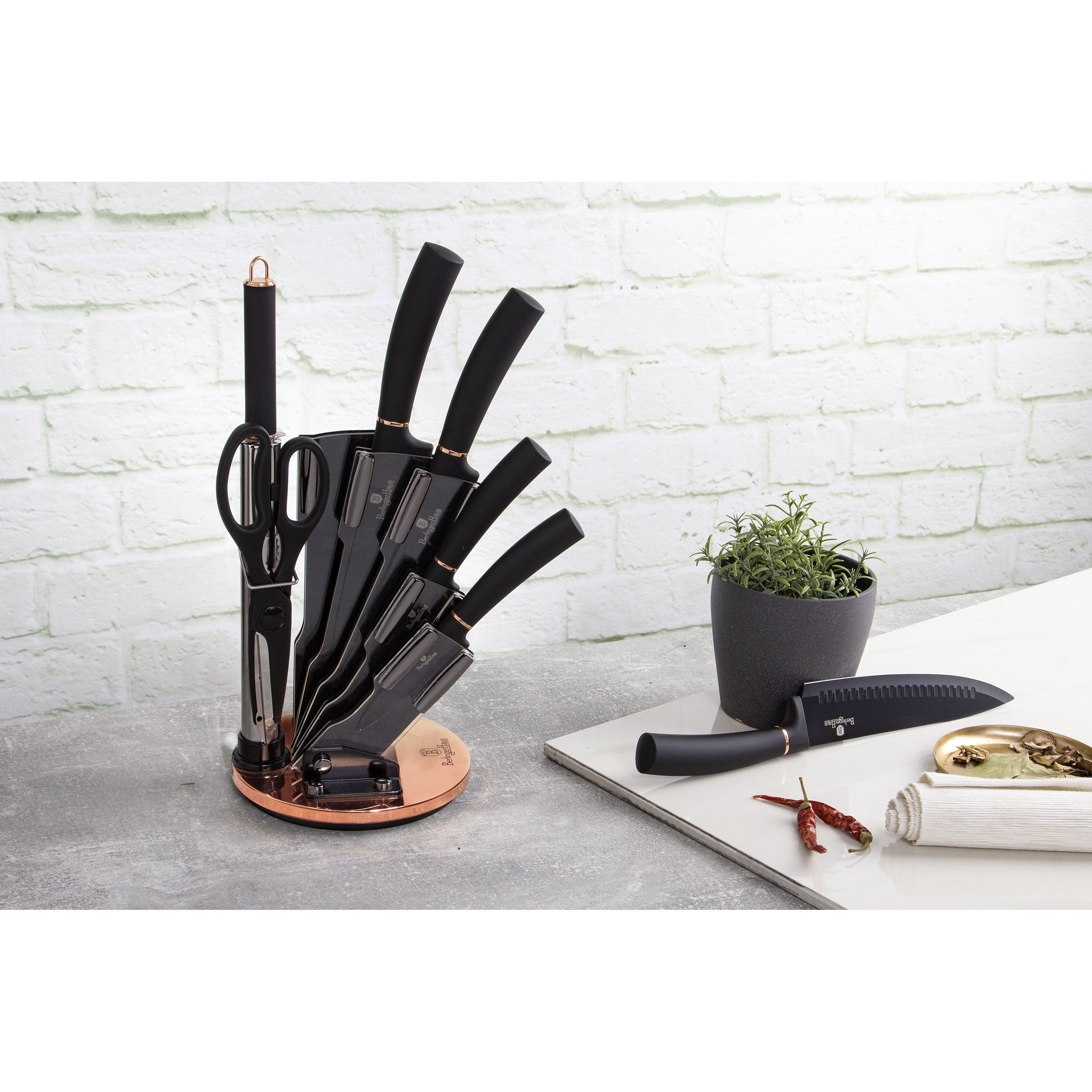 Un juego de cuchillos negros con un soporte, una maceta con una planta y otros artículos de cocina.