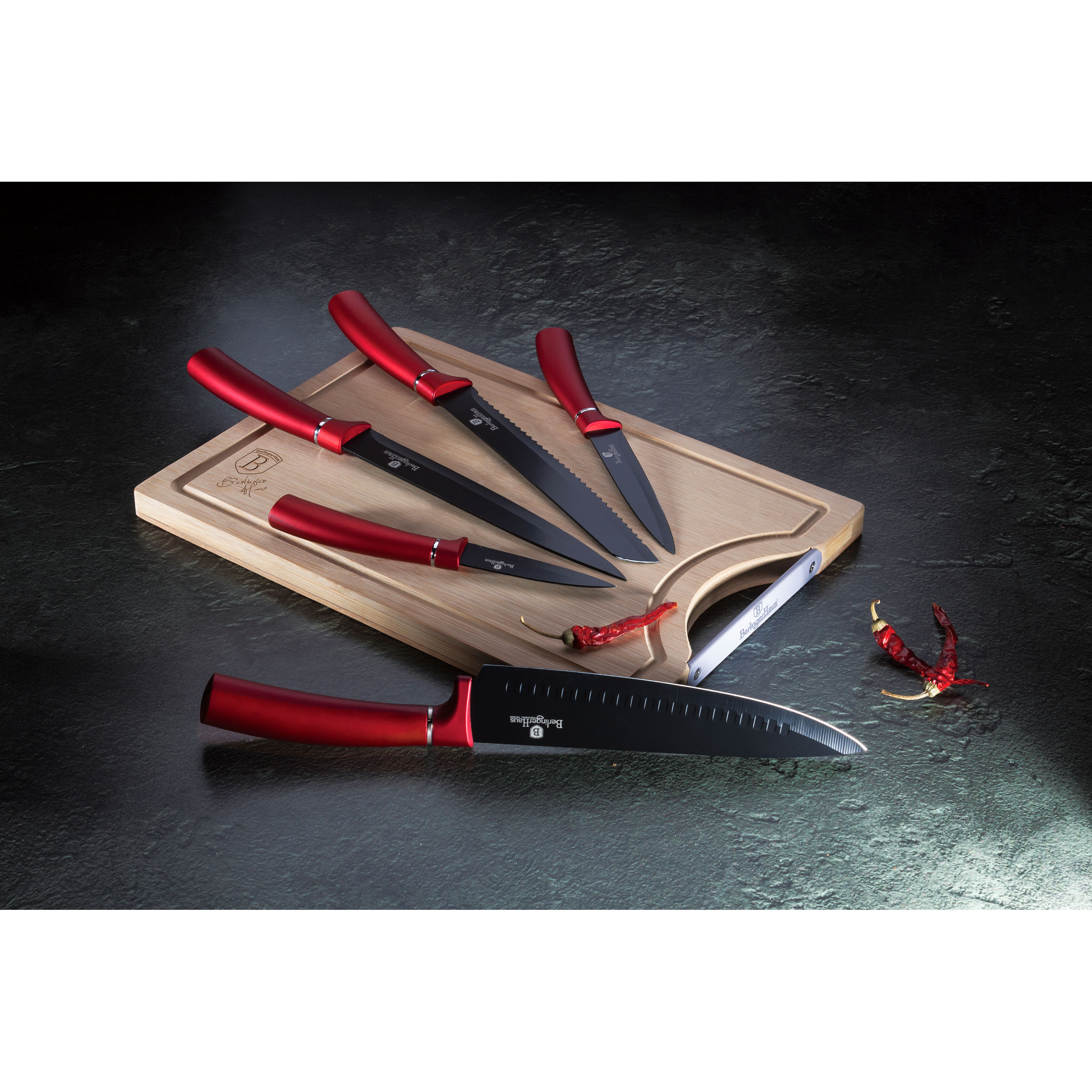 Cuchillos de cocina sobre una tabla de madera con mangos rojos. Chiles rojos a un lado.