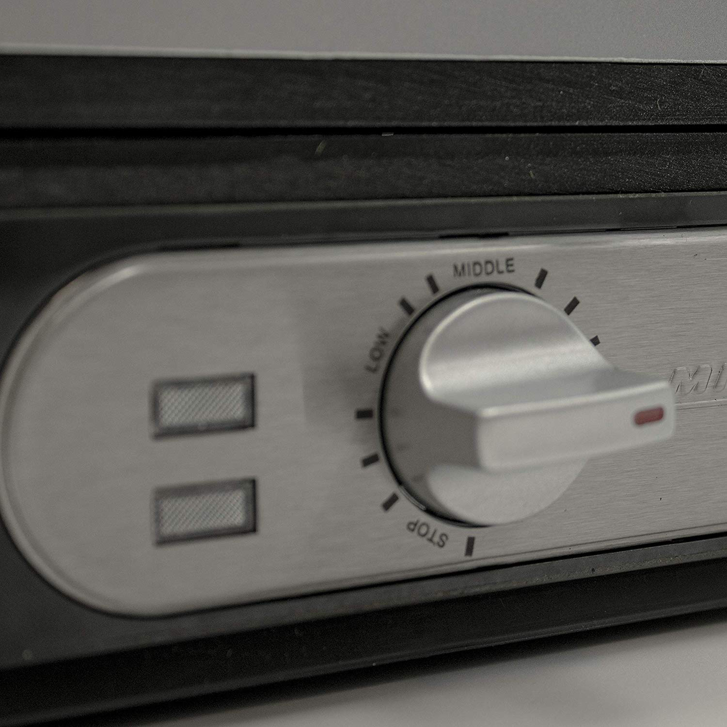 Zbliżenie szczotkowanego metalowego pokrętła z ustawieniami: stop, low, middle. Dwa przyciski obok.