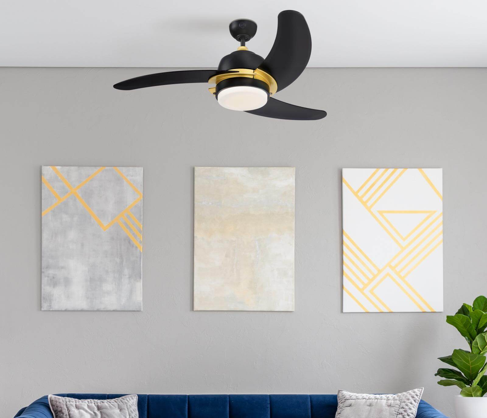 Deckenventilator mit schwarzen Flügeln und goldenen Zierleisten, drei gerahmte abstrakte Kunstwerke und ein blaues Sofa.