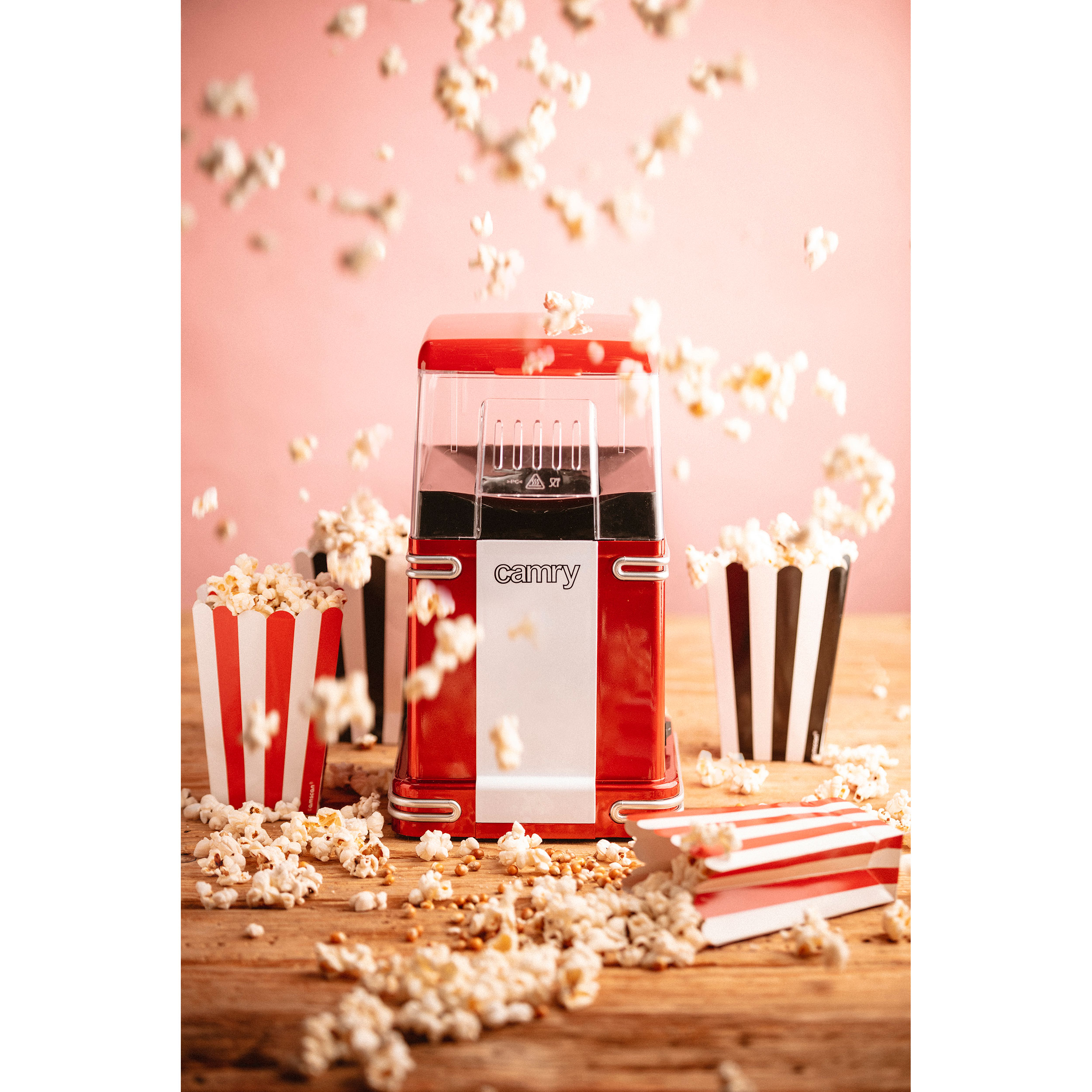 Máquina de palomitas roja con palomitas cayendo, cajas a rayas y palomitas en madera.