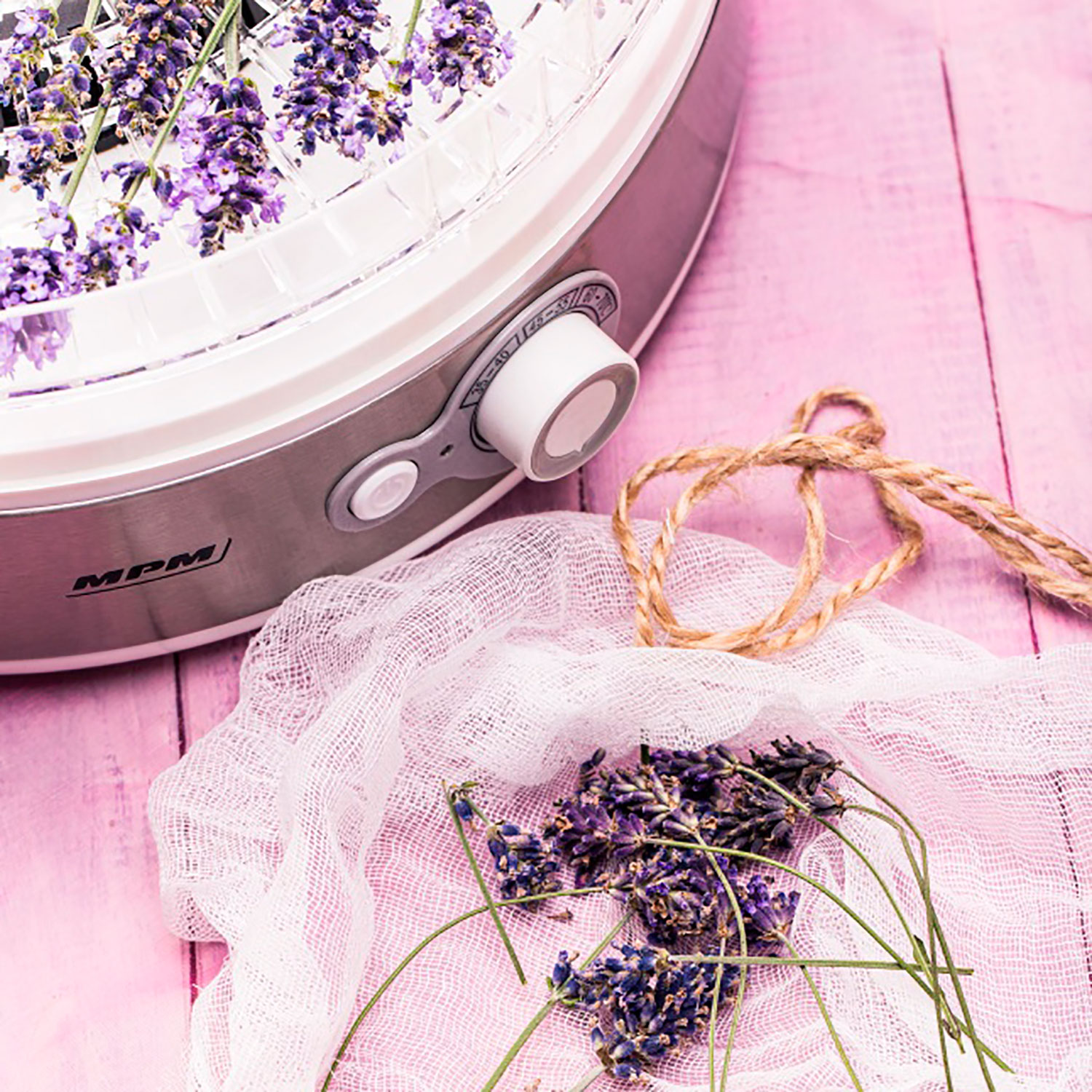 Un deshidratador con lavanda y hilo sobre una superficie de madera rosa.