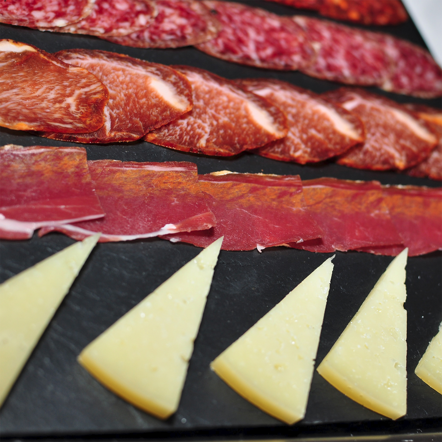 Różne rodzaje plastrowanego mięsa i kawałki sera na czarnej powierzchni. Zbliżenie.