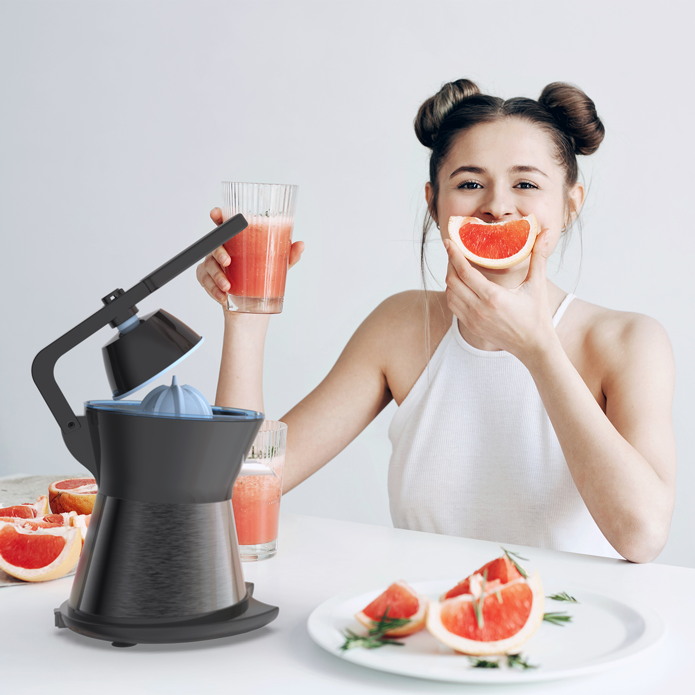 Mujer sosteniendo rodaja de pomelo. Exprimidor a la izquierda, rodajas de pomelo en la mesa, dos vasos de jugo.