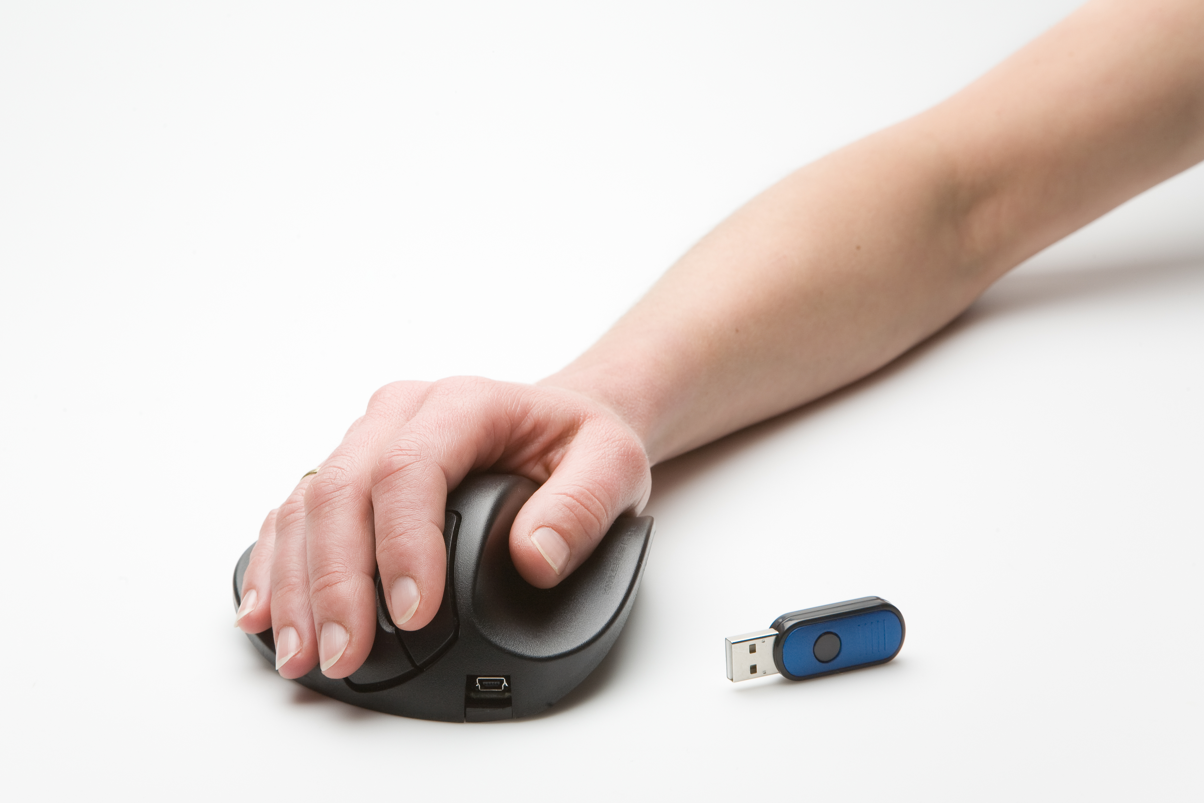 Hand auf schwarzer ergonomischer Maus, USB-Laufwerk in der Nähe, auf weißer Oberfläche.