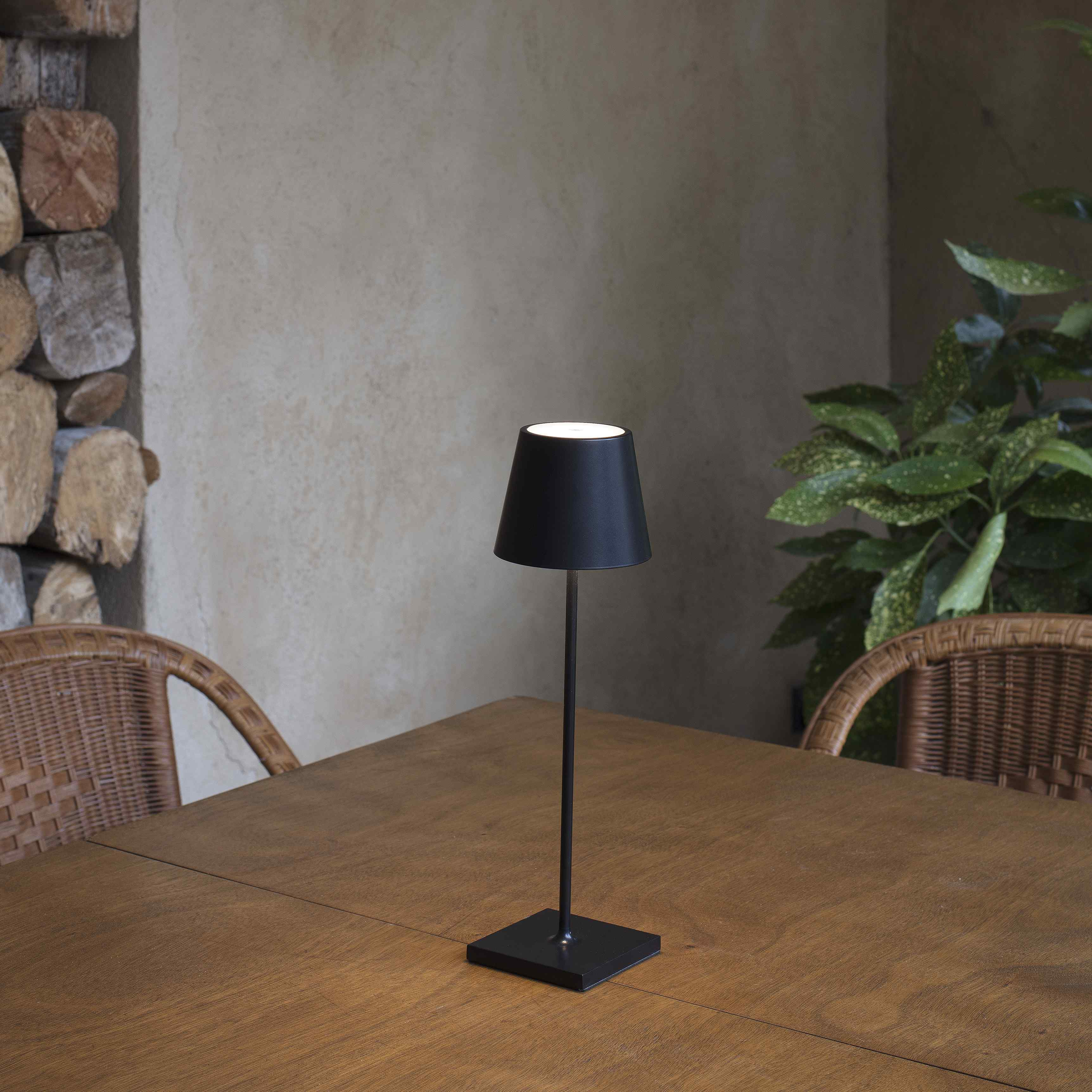 Una piccola lampada nera su un tavolo di legno. Ha un paralume nero e poggia su una base quadrata.