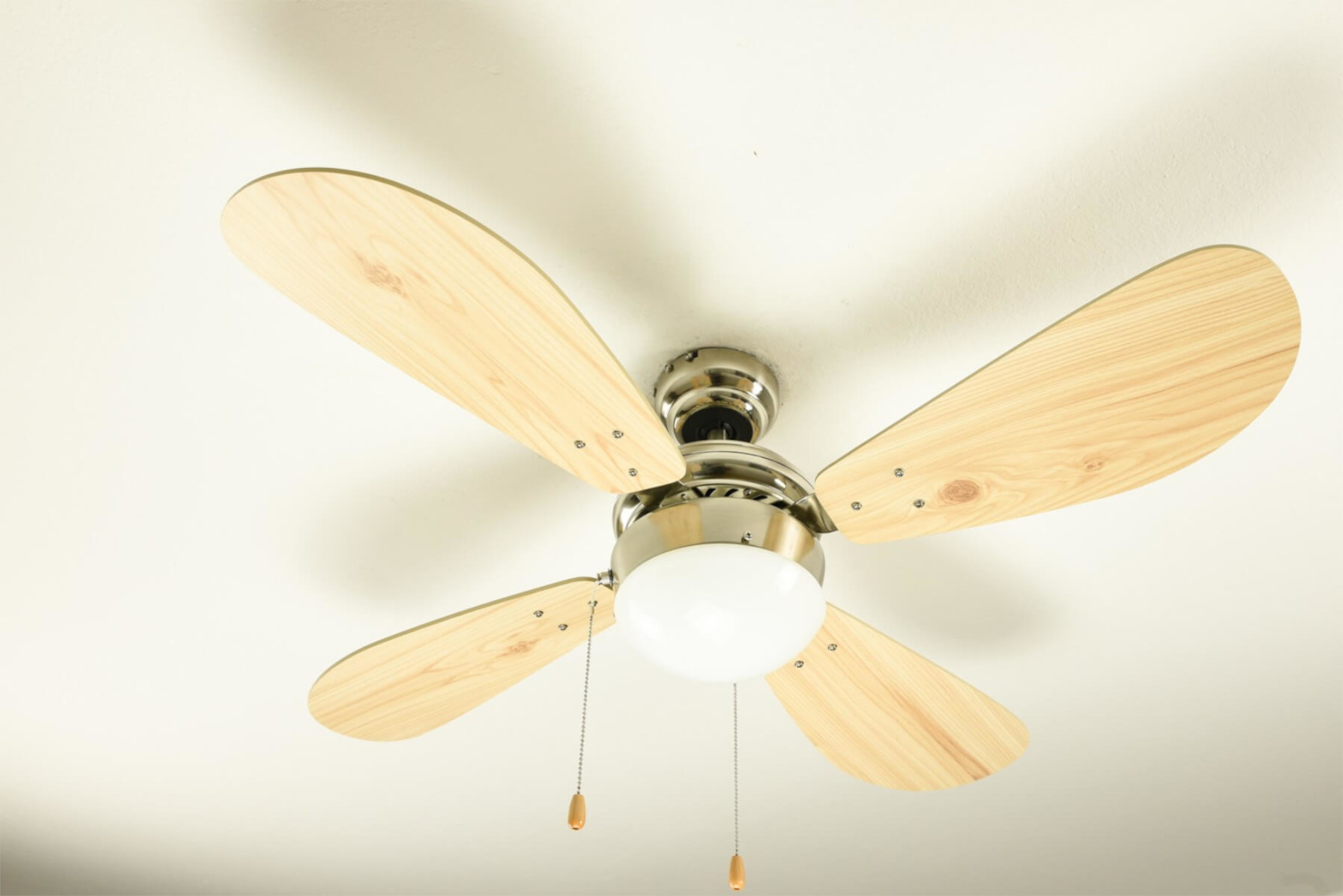 Deckenventilator mit Holzflügeln und zentraler Leuchte vor weißer Decke.