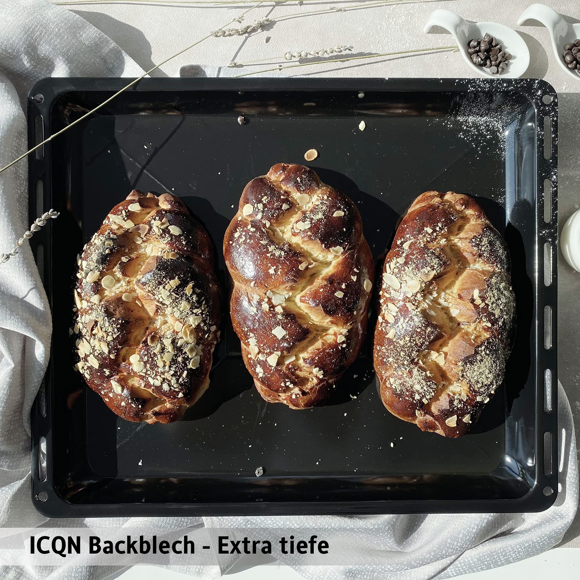 Drei gebackene Brotlaibe auf einem schwarzen Backblech. Samen oben drauf. Weißer Hintergrund.