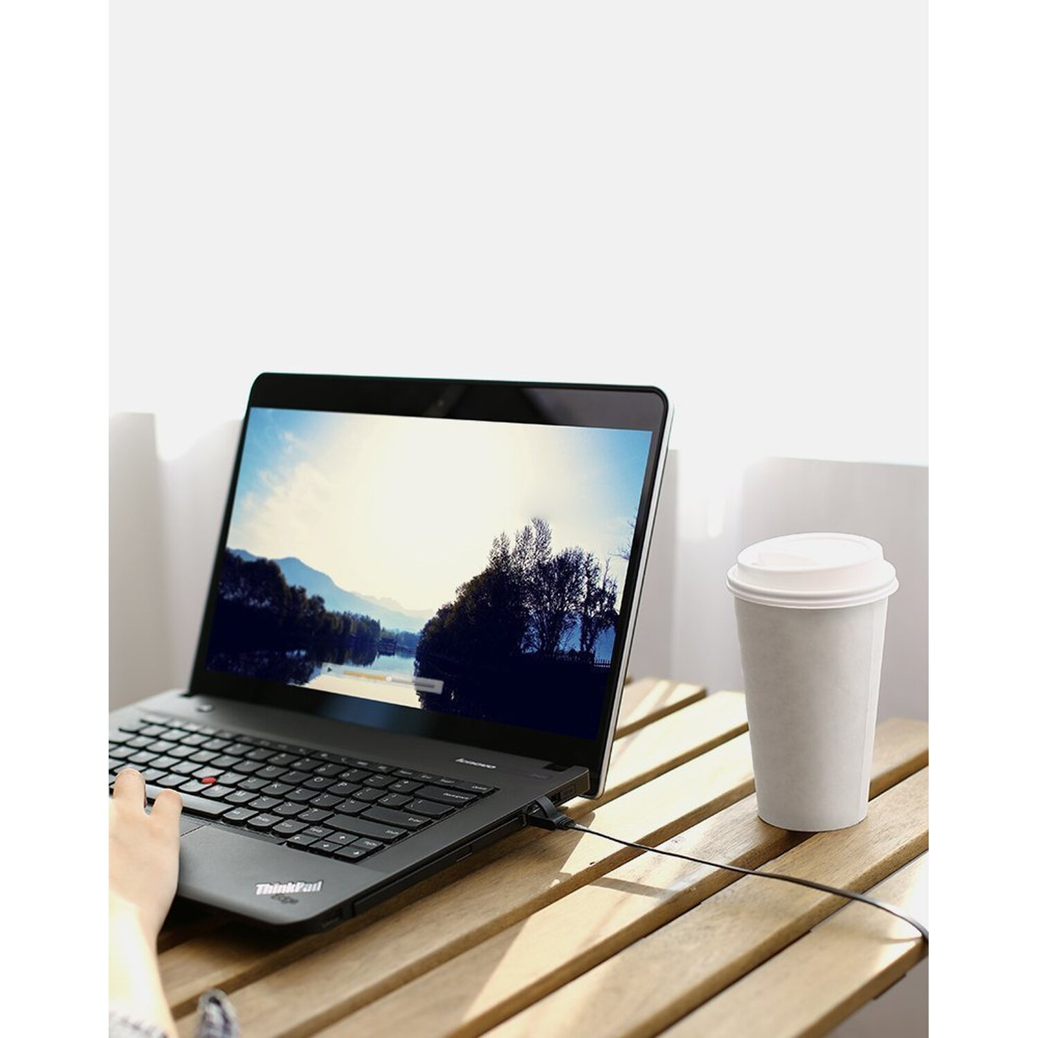 Laptop na drewnianym stole z filiżanką kawy. Osoba korzystająca z laptopa, scena na zewnątrz.