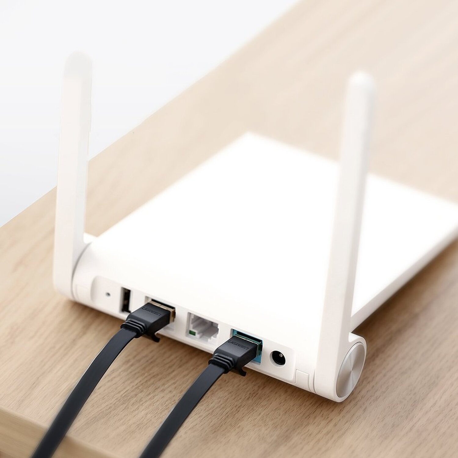 Router bianco con due antenne, collegato a due cavi neri su una superficie in legno.