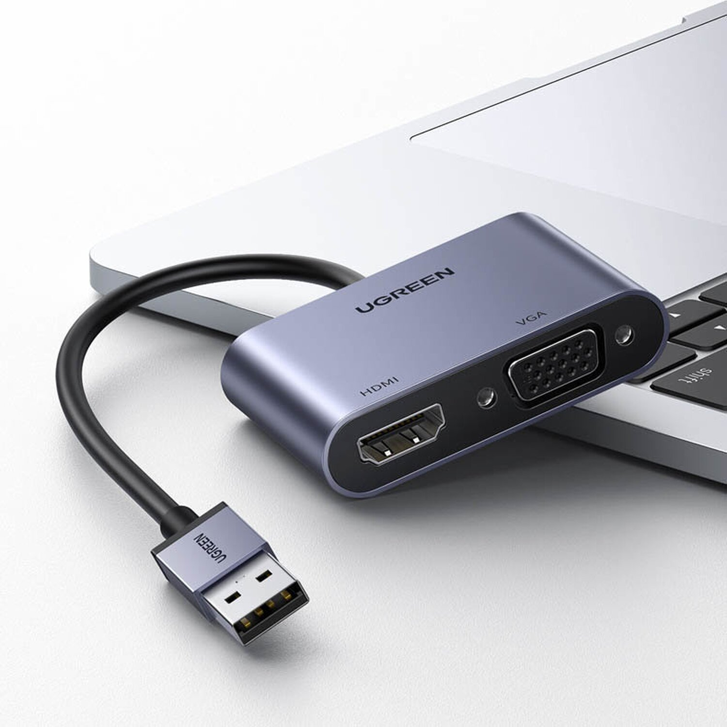Ugreen HDMI-zu-VGA-Adapter, an einen Laptop angeschlossen. Der Adapter ist blau und grau. Weißer Hintergrund.