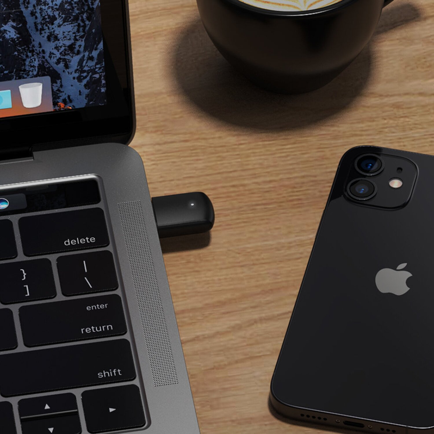 Laptop z kluczem USB-C i czarnym iPhonem na drewnianym biurku z filiżanką kawy.