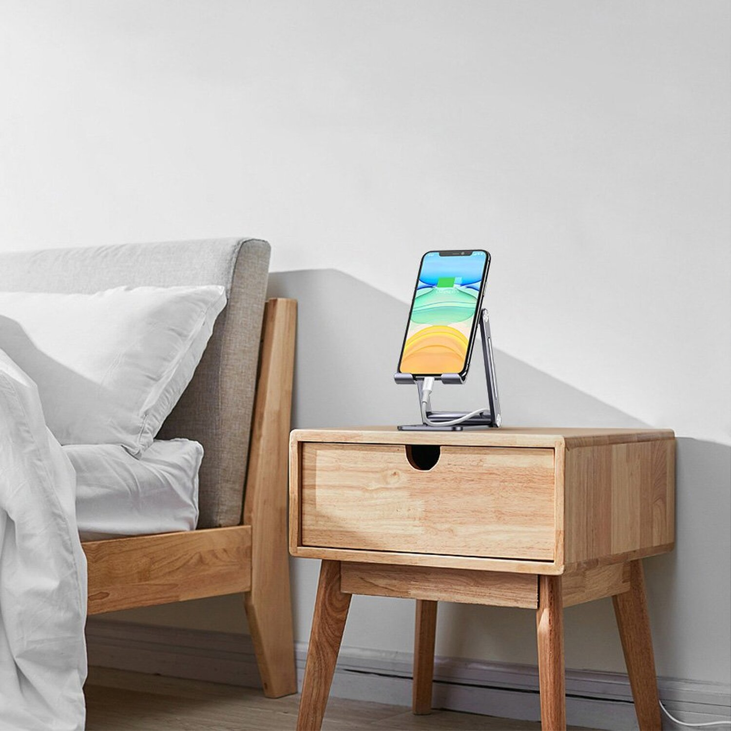 Ein Telefon steht auf einem Ständer auf einem hölzernen Nachttisch neben einem Bett. Weißer Hintergrund.
