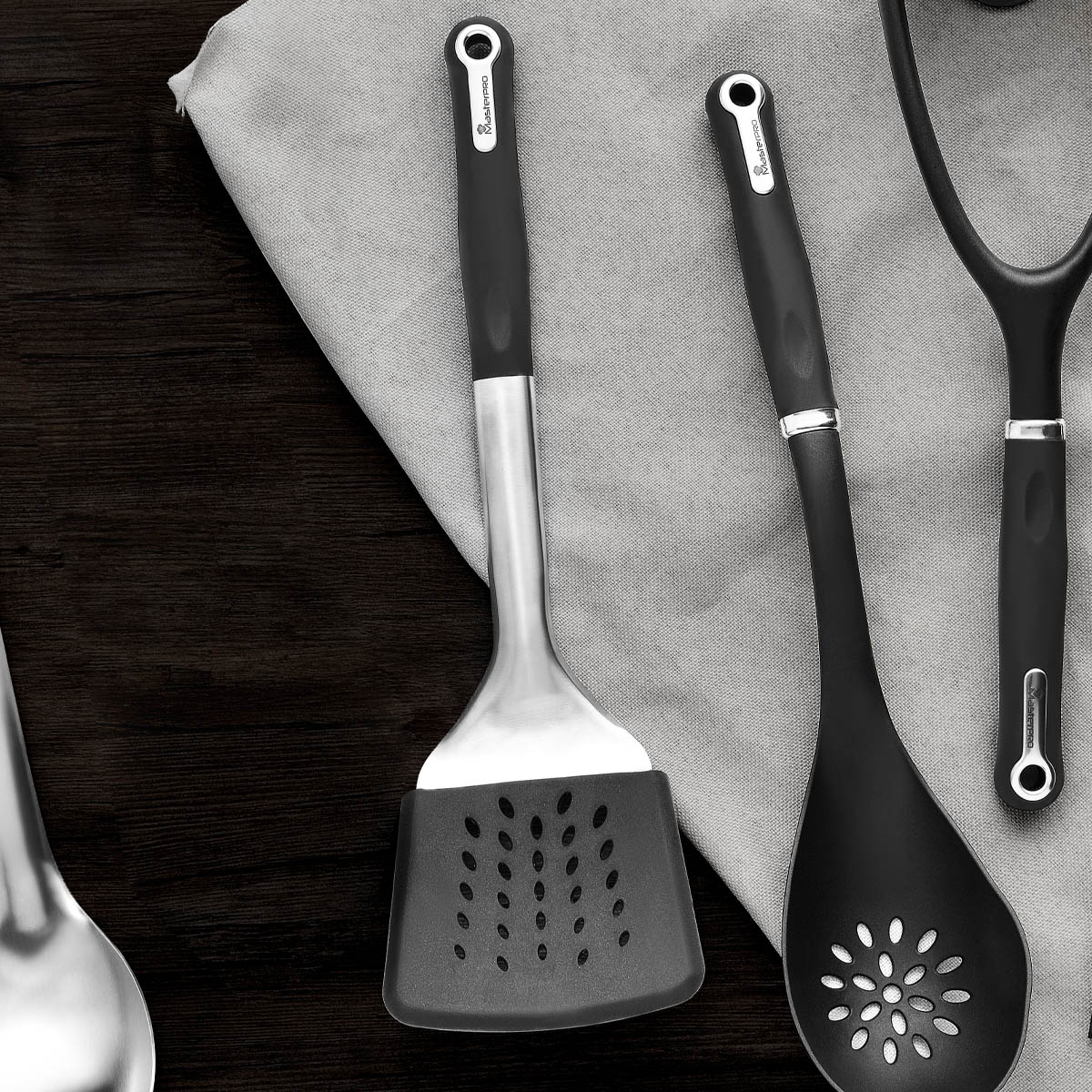 Mutfak eşyaları: oluklu spatula, kaşık ve patates ezici, gri bir bez üzerinde.