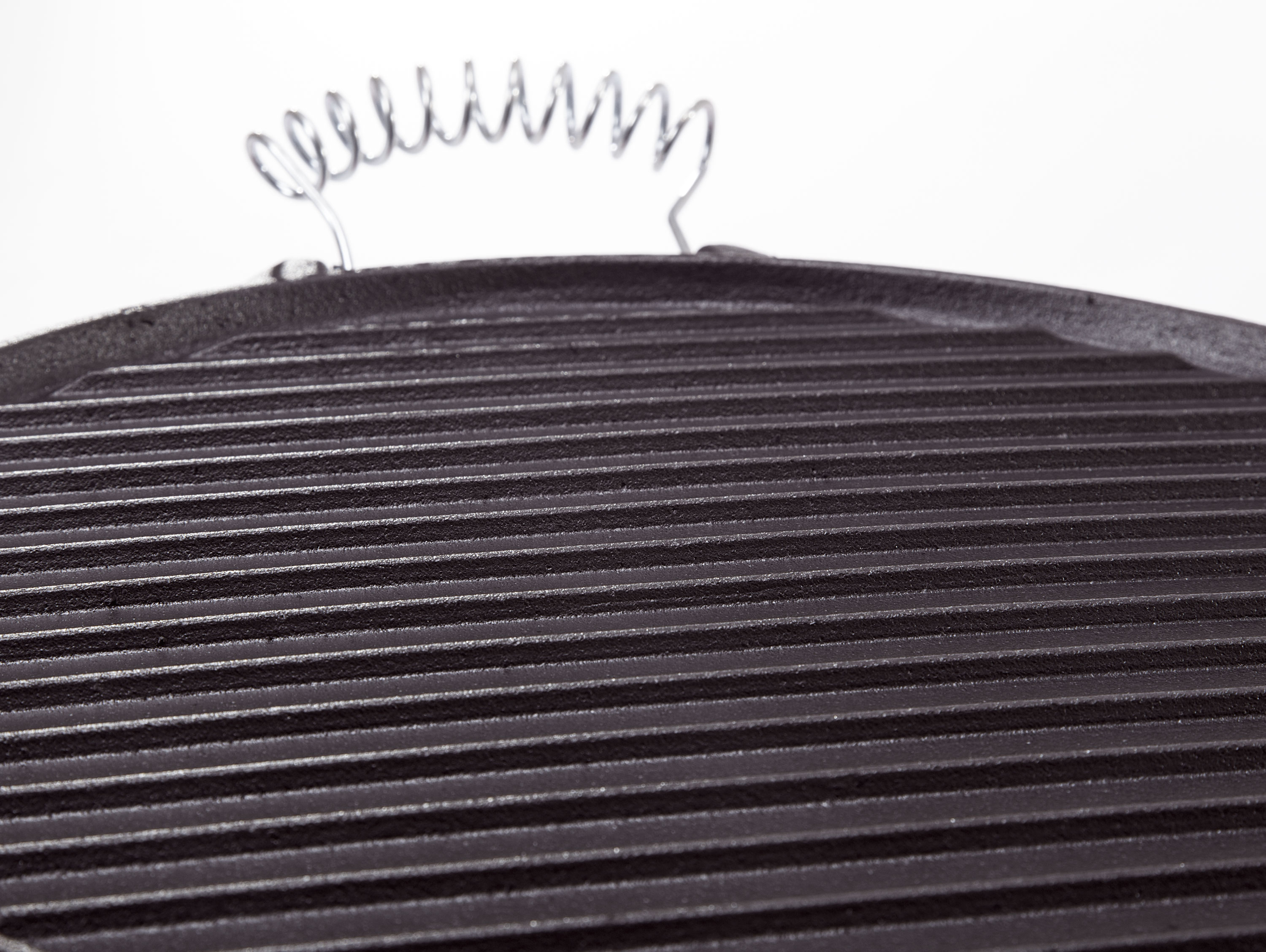 Nahaufnahme einer schwarzen Grillpfanne aus Gusseisen mit Rillen und einem spiralförmigen Griff.