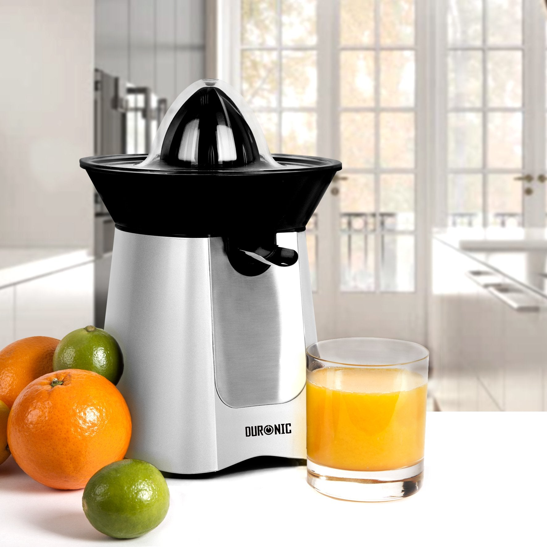Exprimidor plateado y negro con naranjas y limas, y un vaso de zumo de naranja.