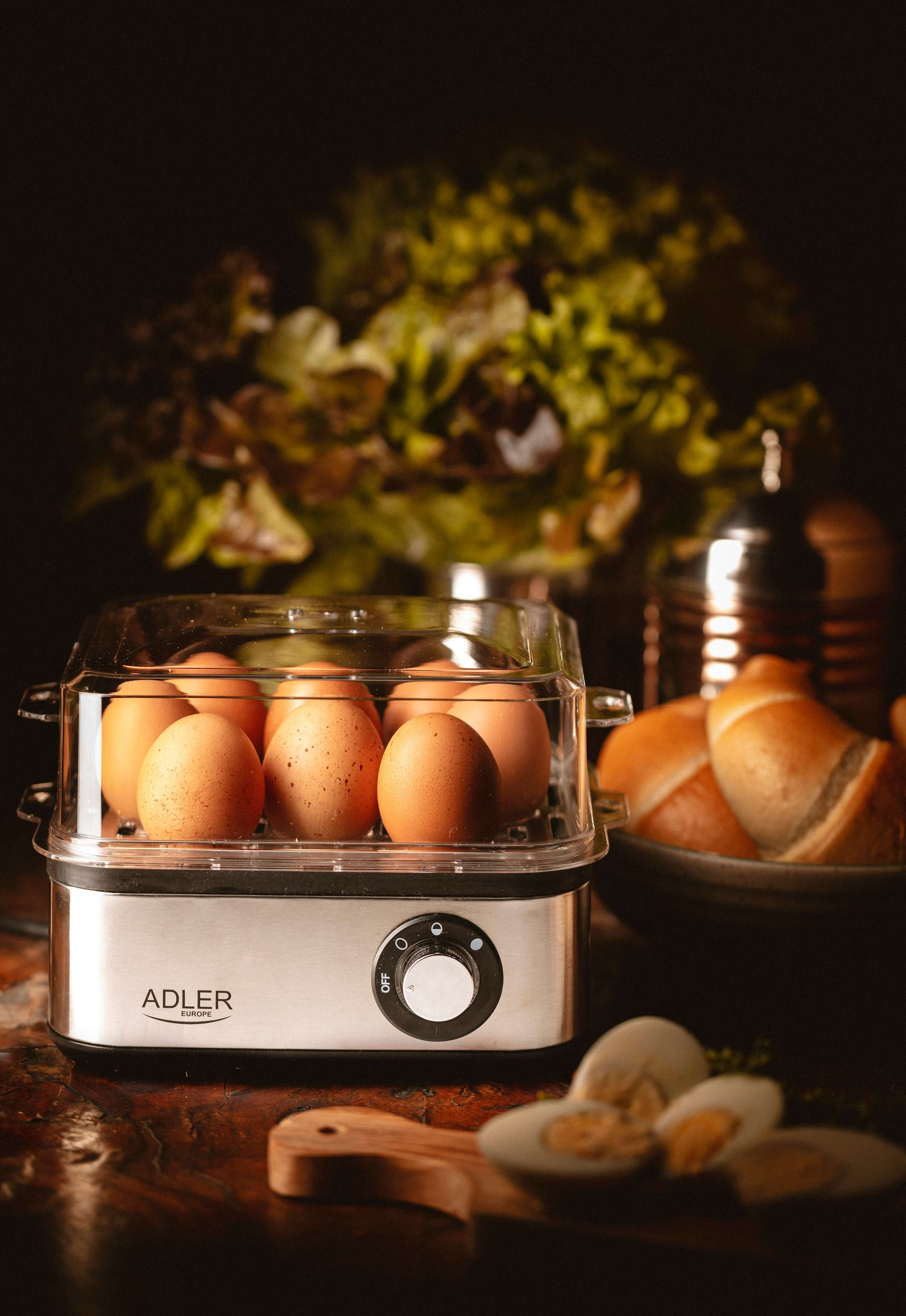 Gotowacz do jajek z jajkami w środku. W tle znajduje się chleb, sałatka i inne produkty spożywcze.