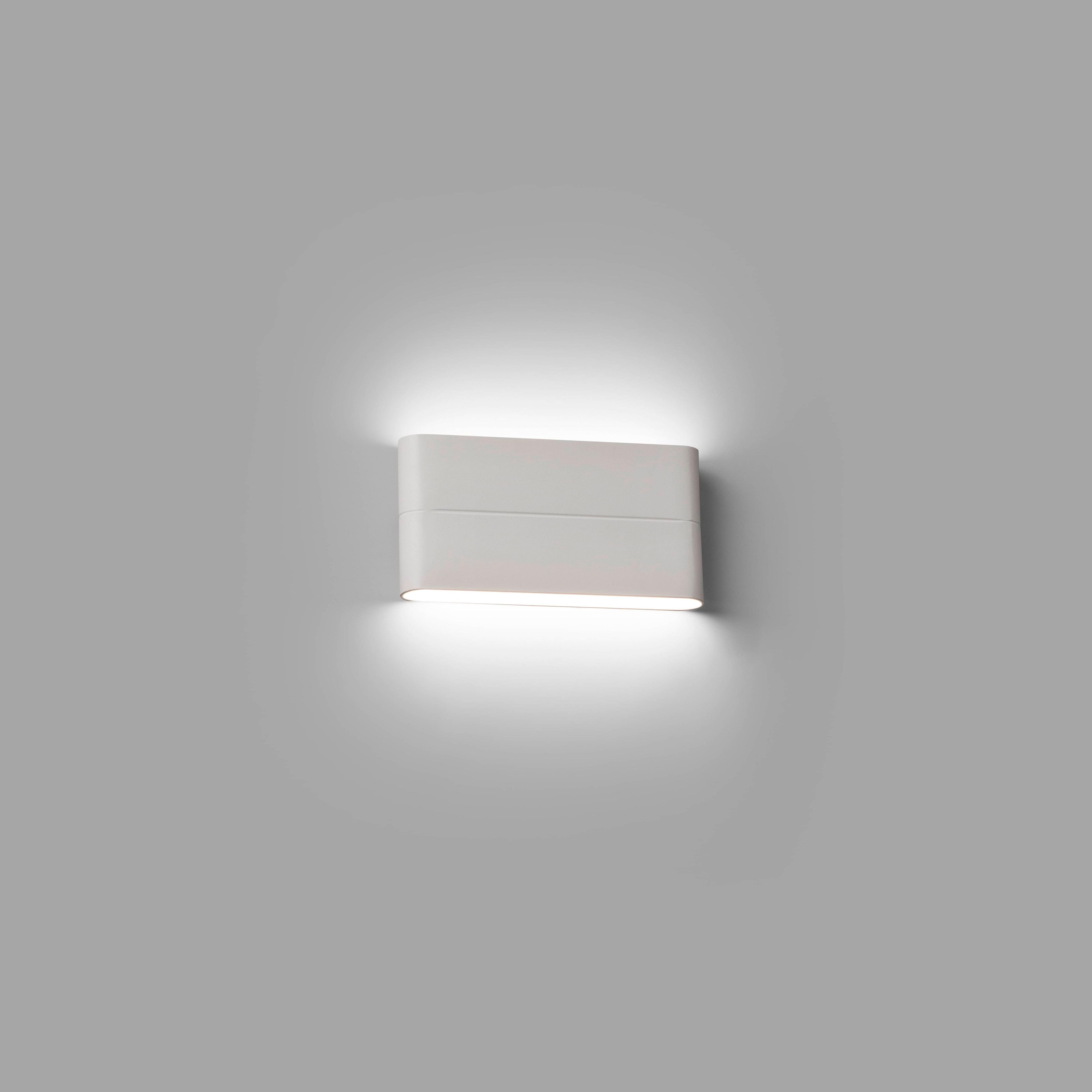 Una moderna lampada da parete con una luce intensa che brilla verso il basso su un muro grigio.