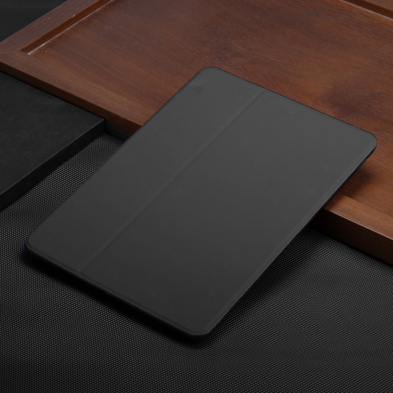 Eine schwarze Tablet-Hülle auf einer dunklen Holzoberfläche. Die Hülle ist geschlossen und liegt schräg.