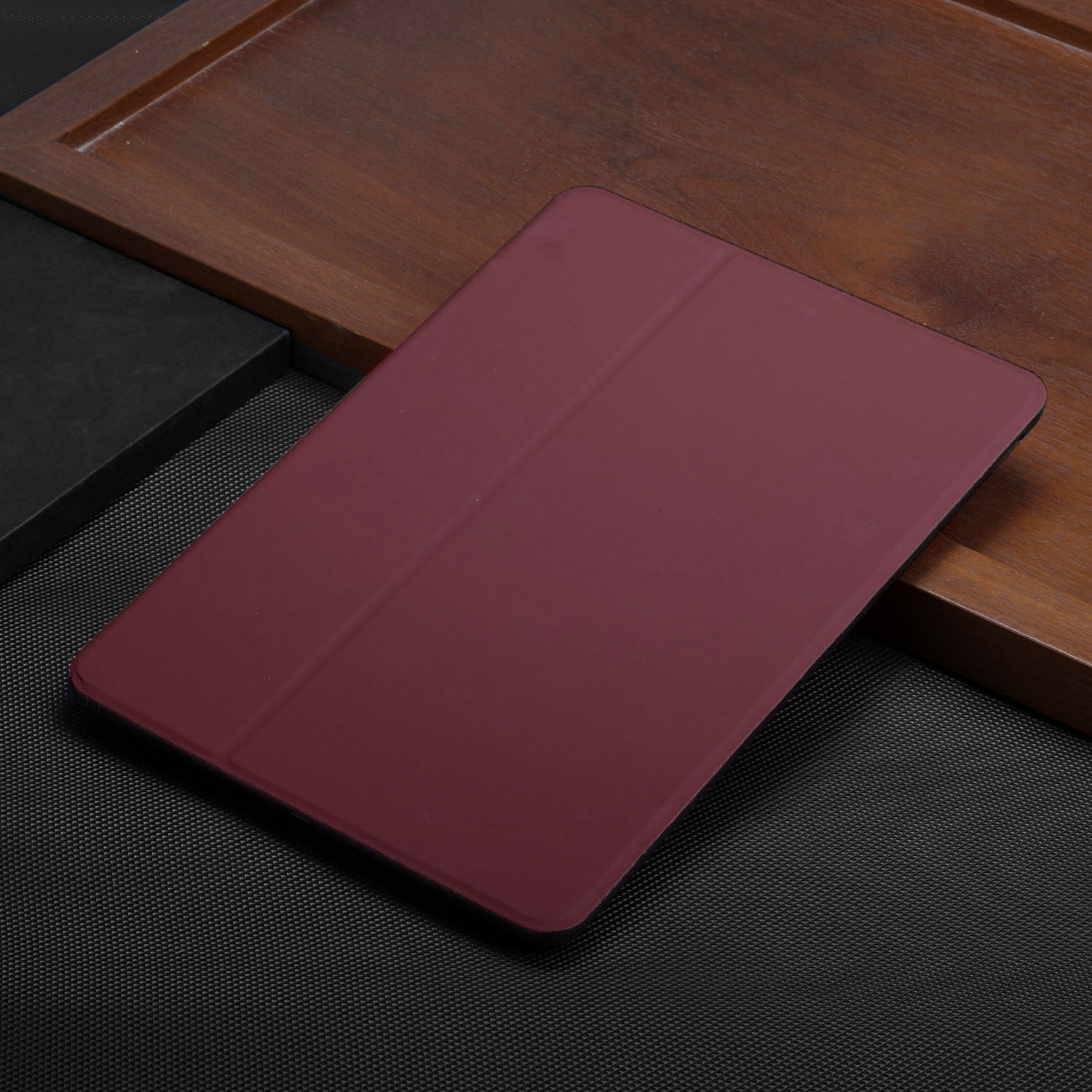 Eine Tablet-Hülle, weinrot, liegt auf einer Holzoberfläche.