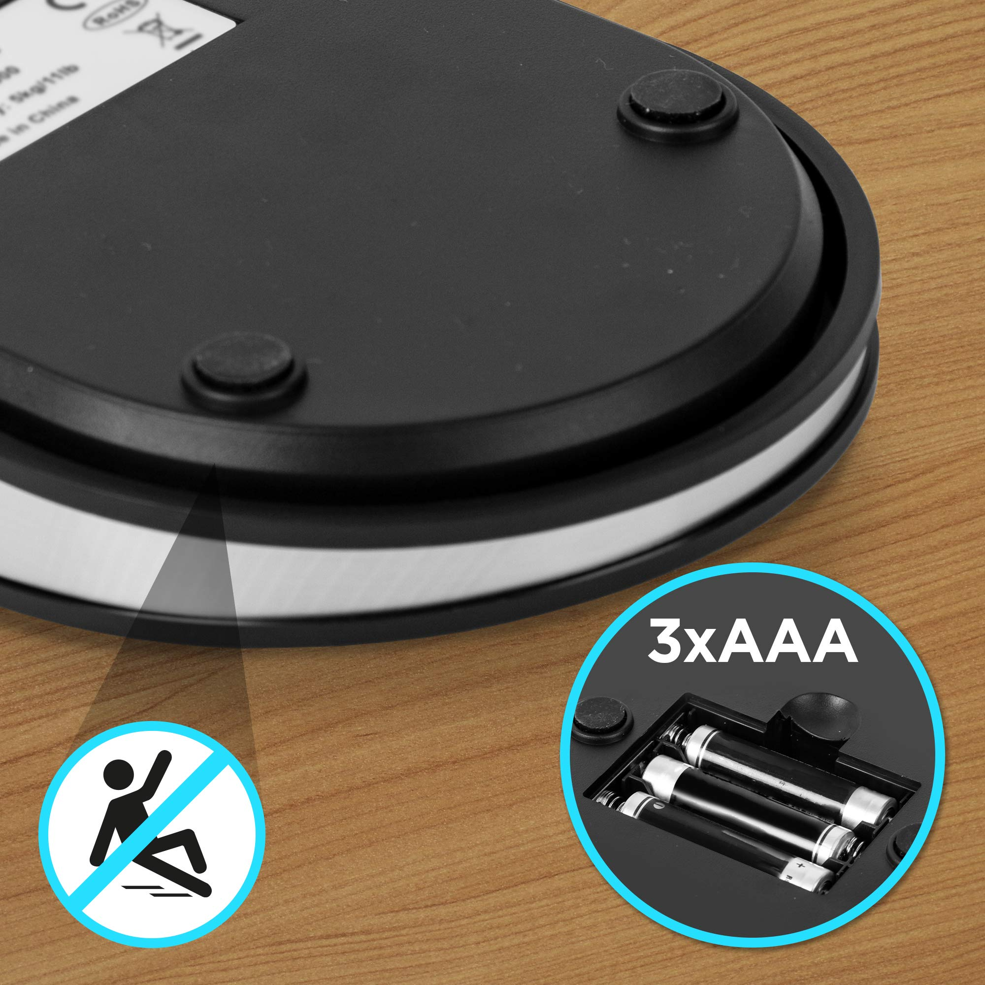 Unterseite einer schwarz-silbernen Waage mit Batteriefach und einem Sturzverbot-Zeichen.
