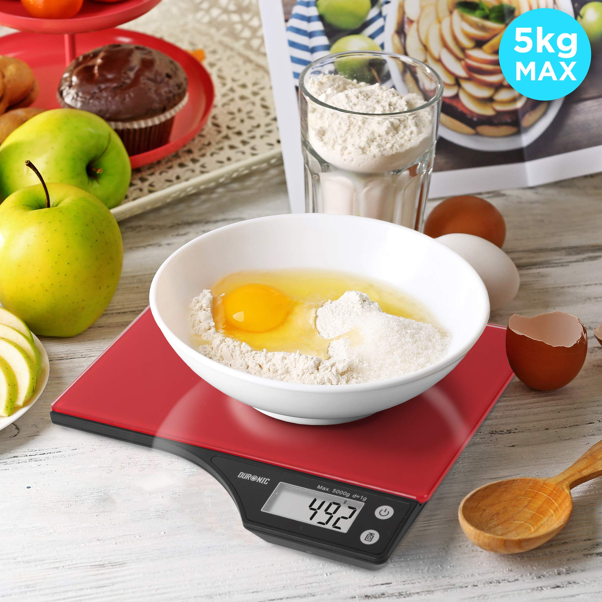 Báscula de cocina digital roja con ingredientes en un bol. Un bol contiene huevos, harina y azúcar, con fruta cerca.