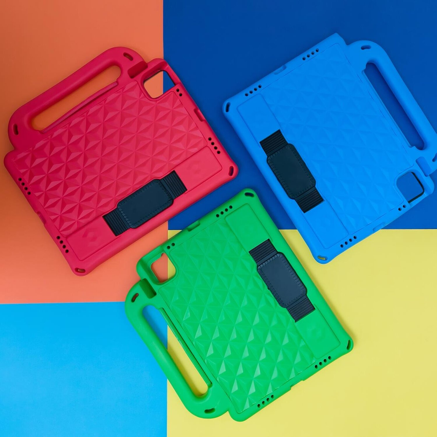 Drei bunte Tablethüllen, rot, blau und grün, auf blau-gelbem Hintergrund angeordnet.