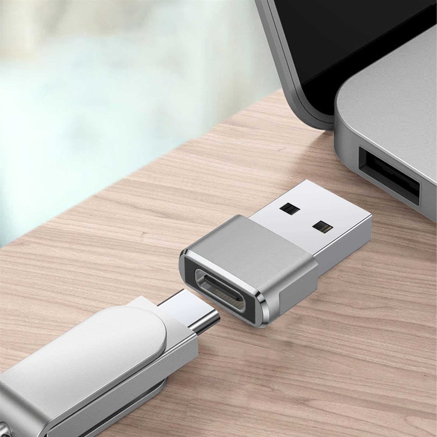 Un adaptador USB-C a USB plateado conectado a un cable USB, sobre una superficie de madera.