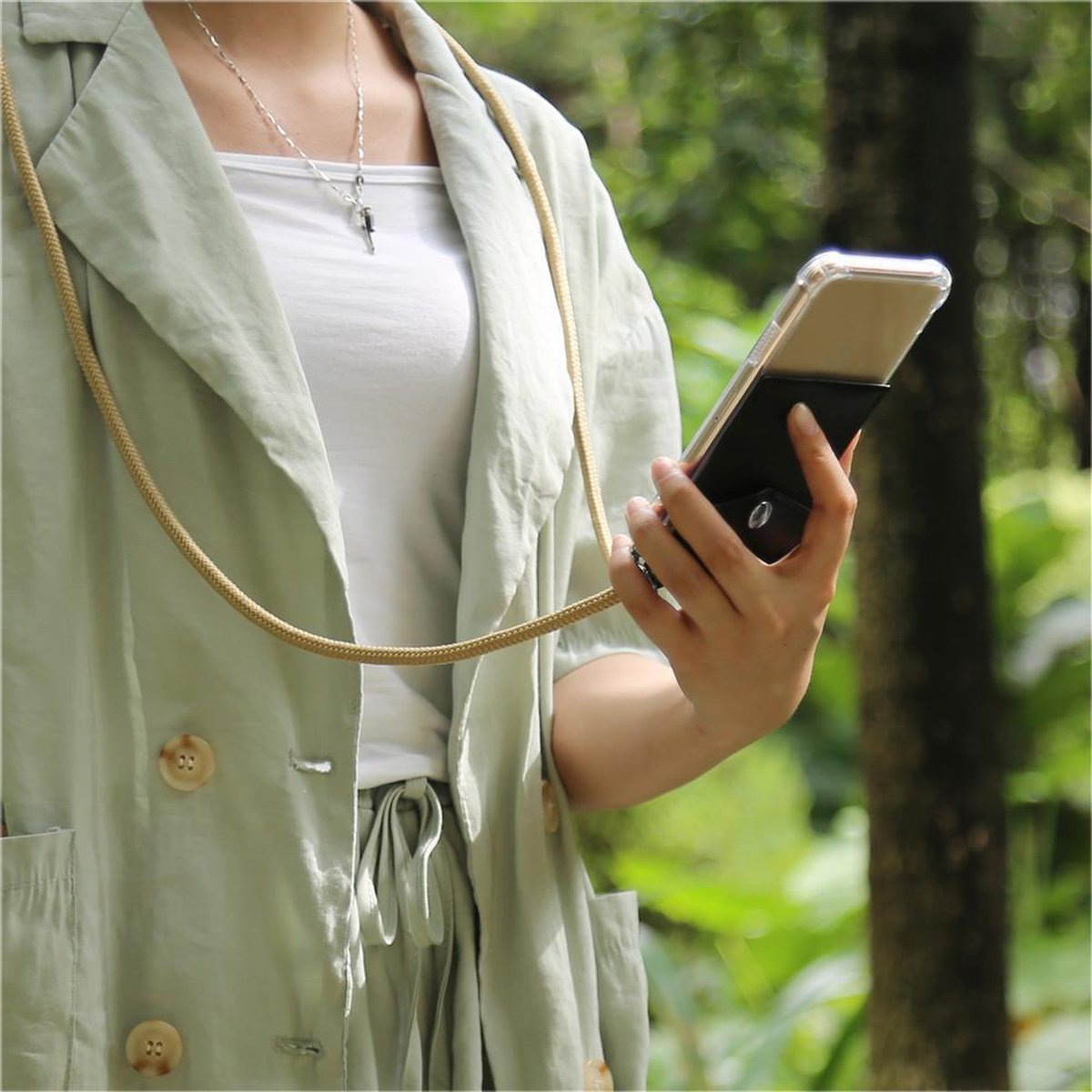Donna che tiene il telefono con cordino. Cordino beige. Giacca verde e camicia bianca. Natura.