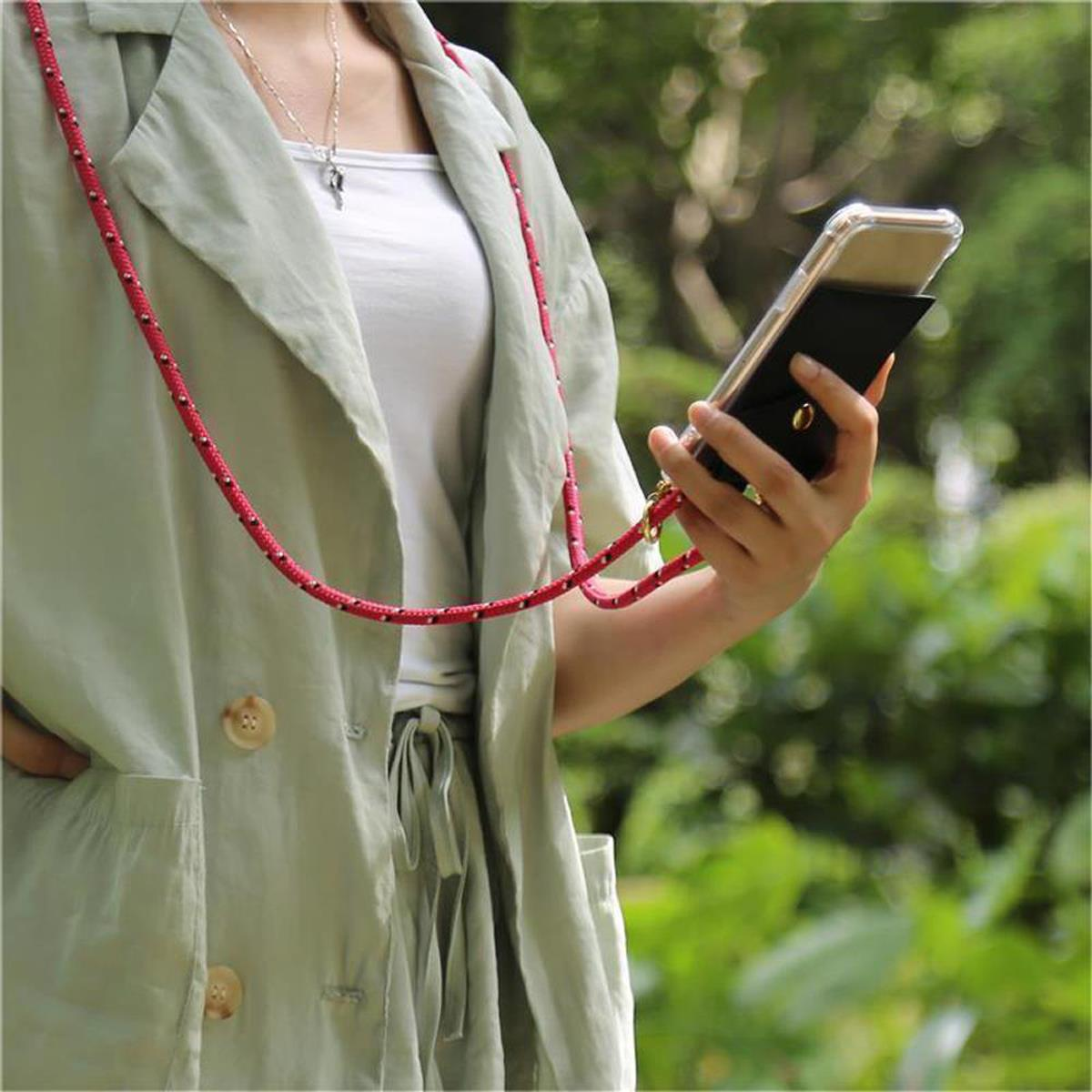 Donna che tiene in mano un telefono in una custodia nera con un cordino rosso. Indossa una giacca verde. Sfondo verde.